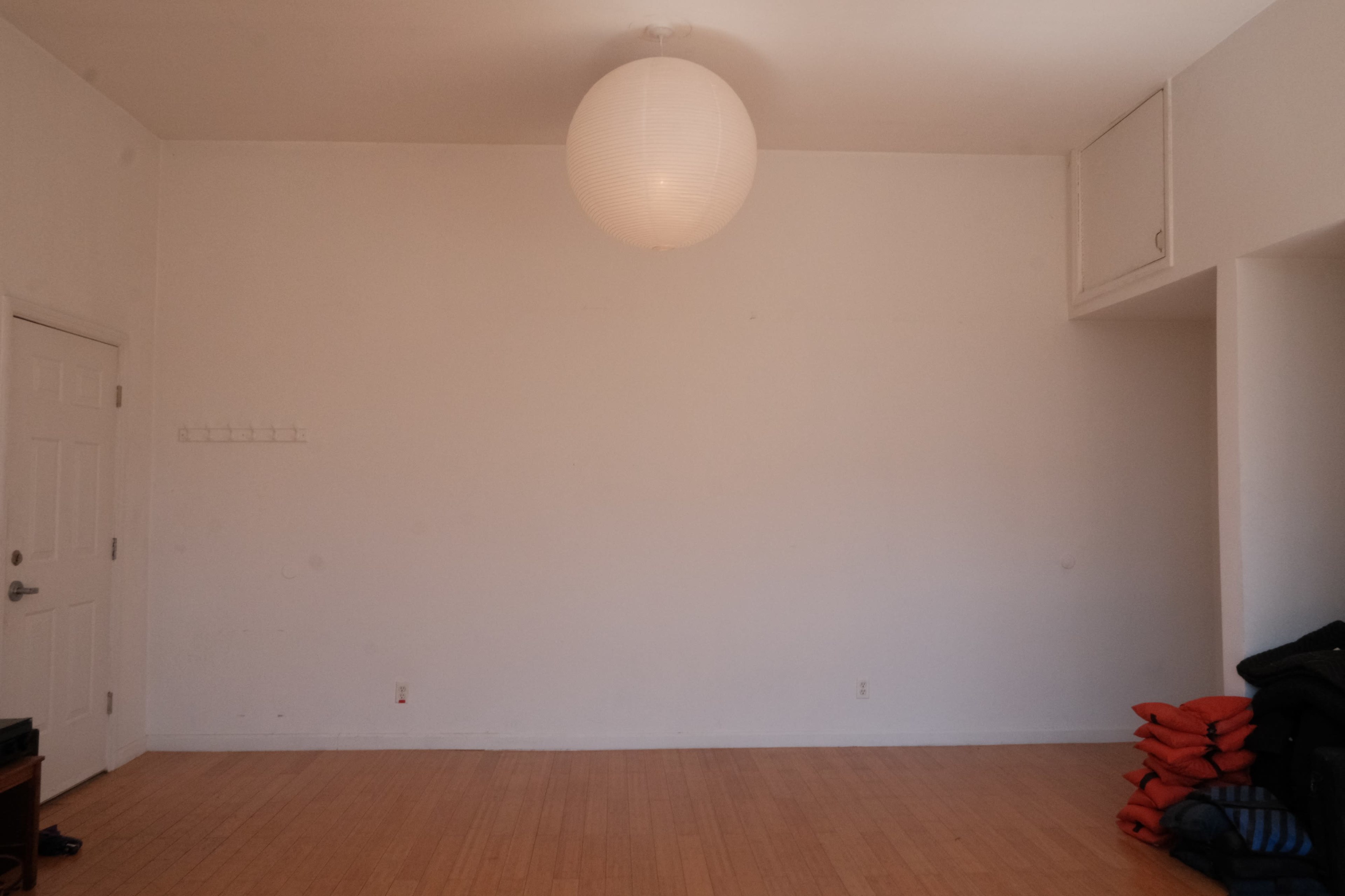 An empty room with a large paper lantern hanging from the ceiling and stacked blankets in one corner.