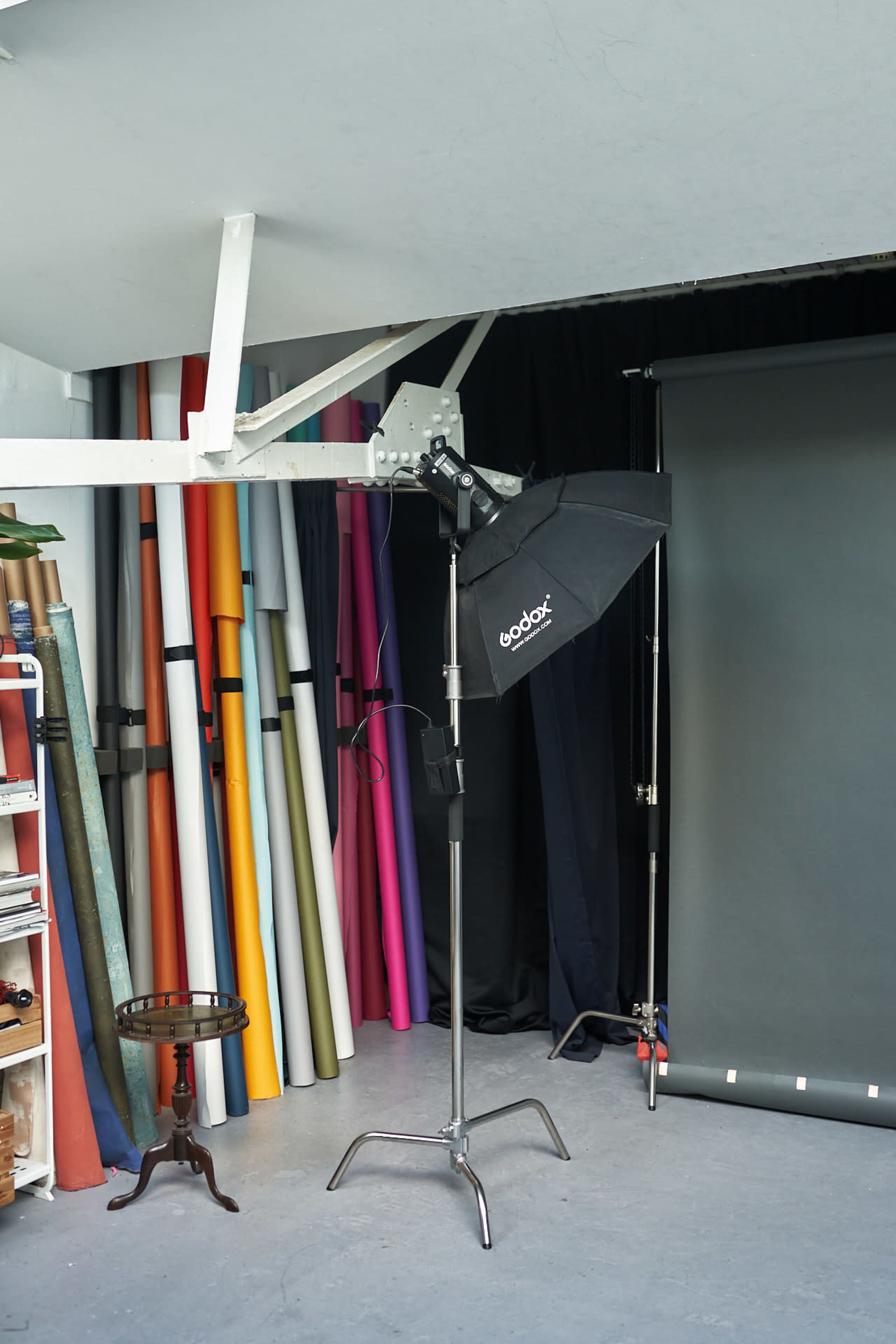 A photography studio setup with a light stand, softbox, and a variety of colorful backdrop rolls behind it.