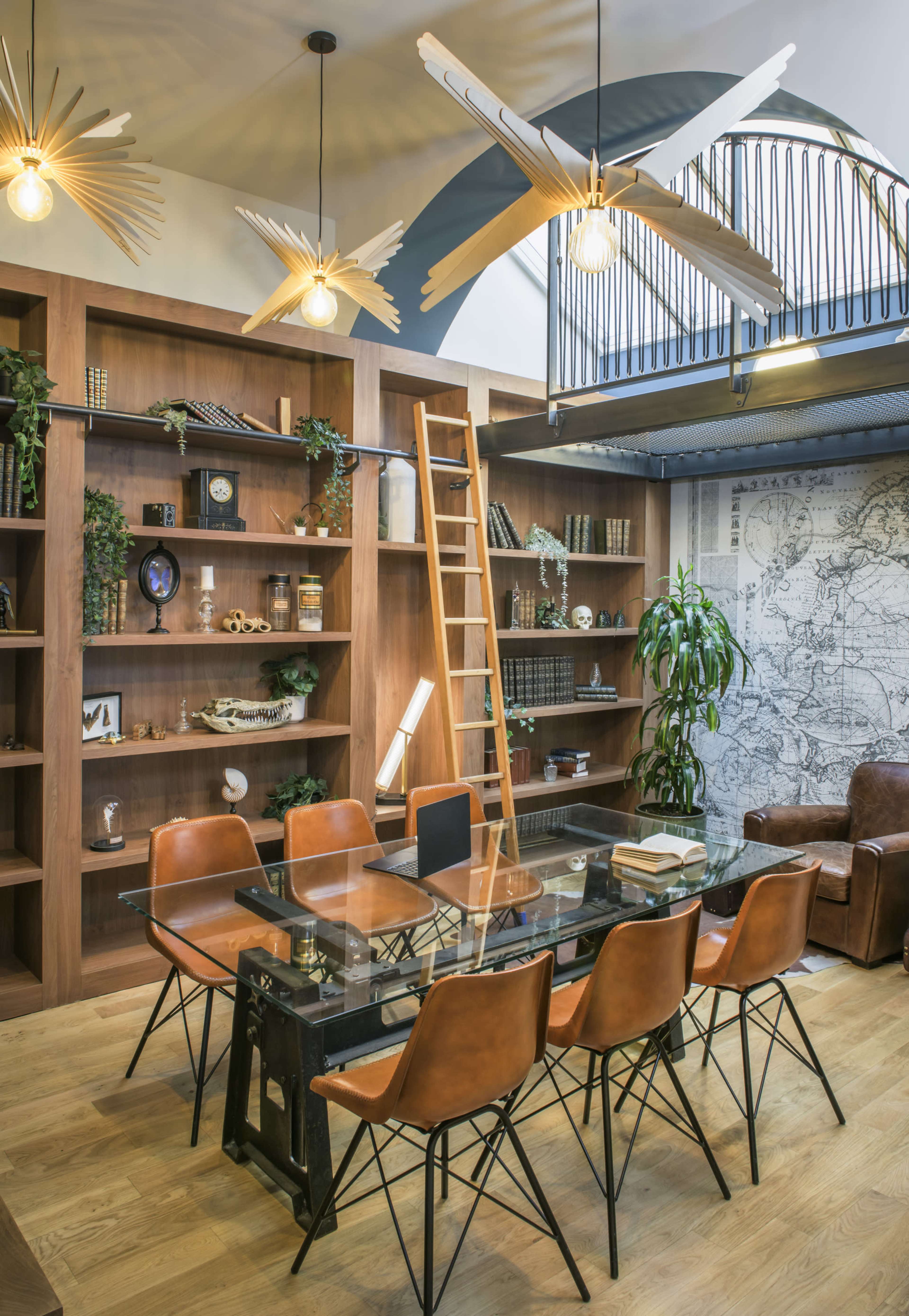 A spacious interior features a dining area with a glass table surrounded by six leather chairs, wooden shelves lined with decor, and a ladder leading to an upper level.