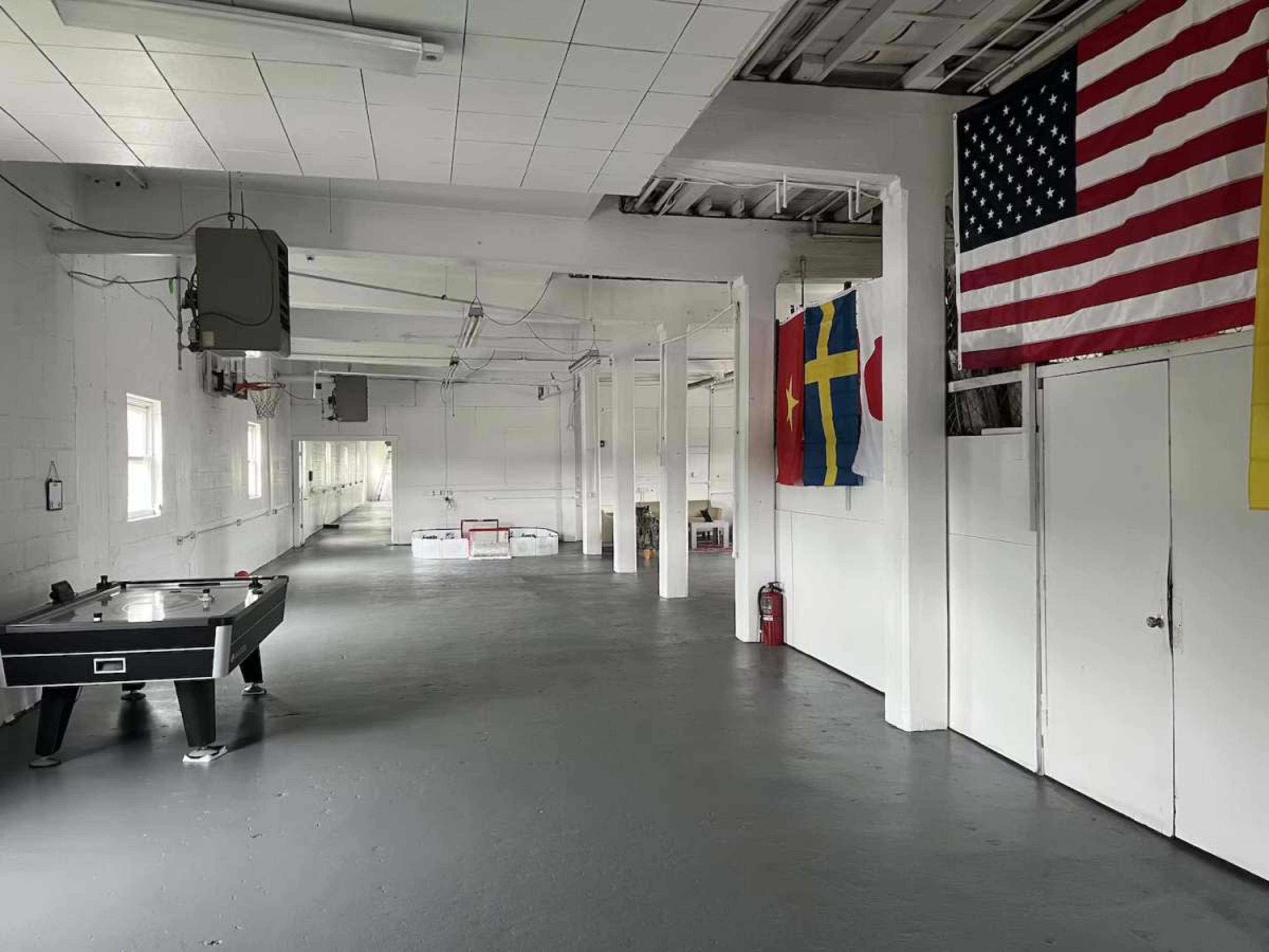 The image shows a large, empty indoor space with a pool table, several flags on the walls, and a white painted floor.