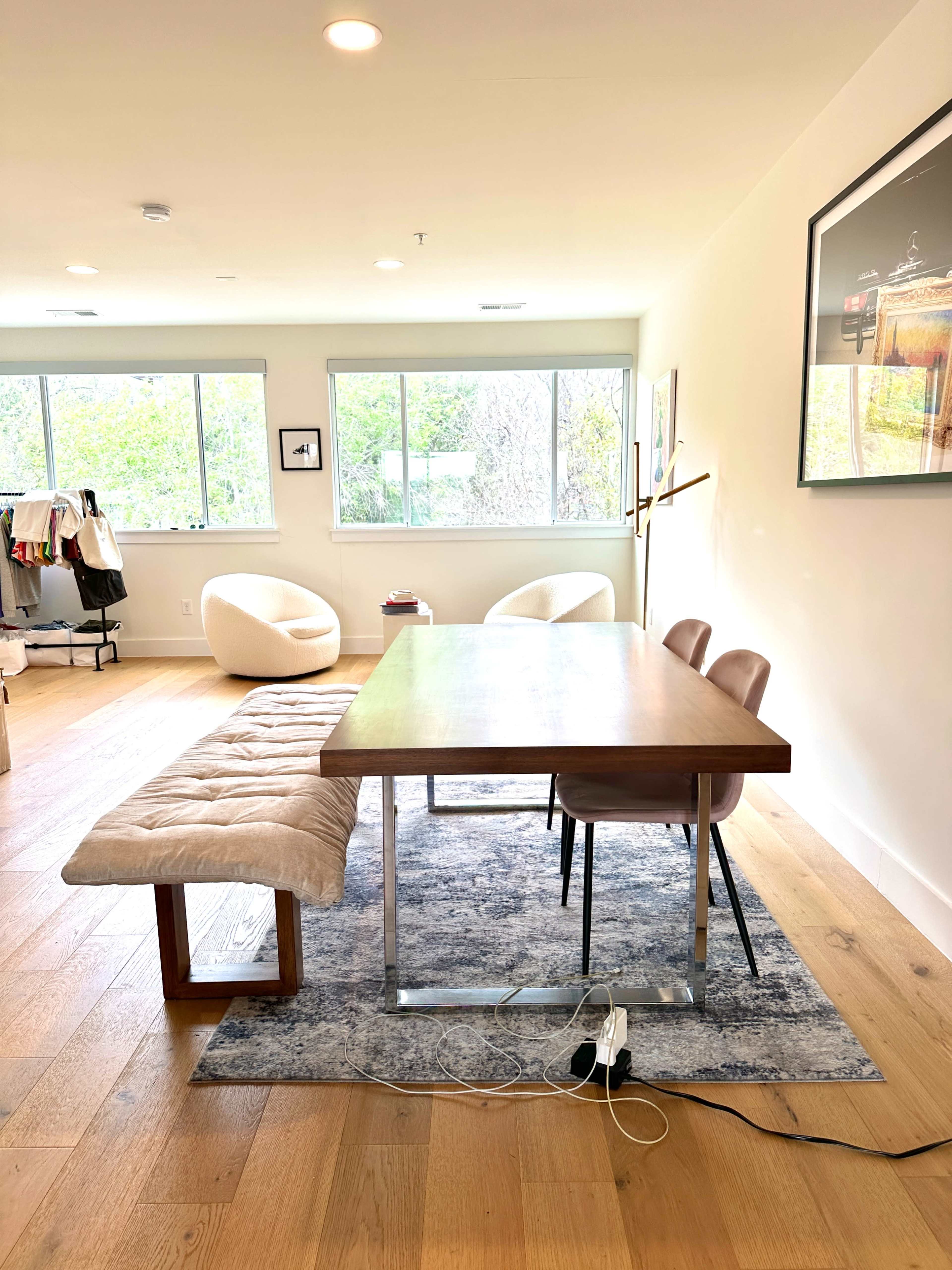 A modern dining area features a wooden table with a bench and two chairs on a patterned rug, surrounded by large windows.
