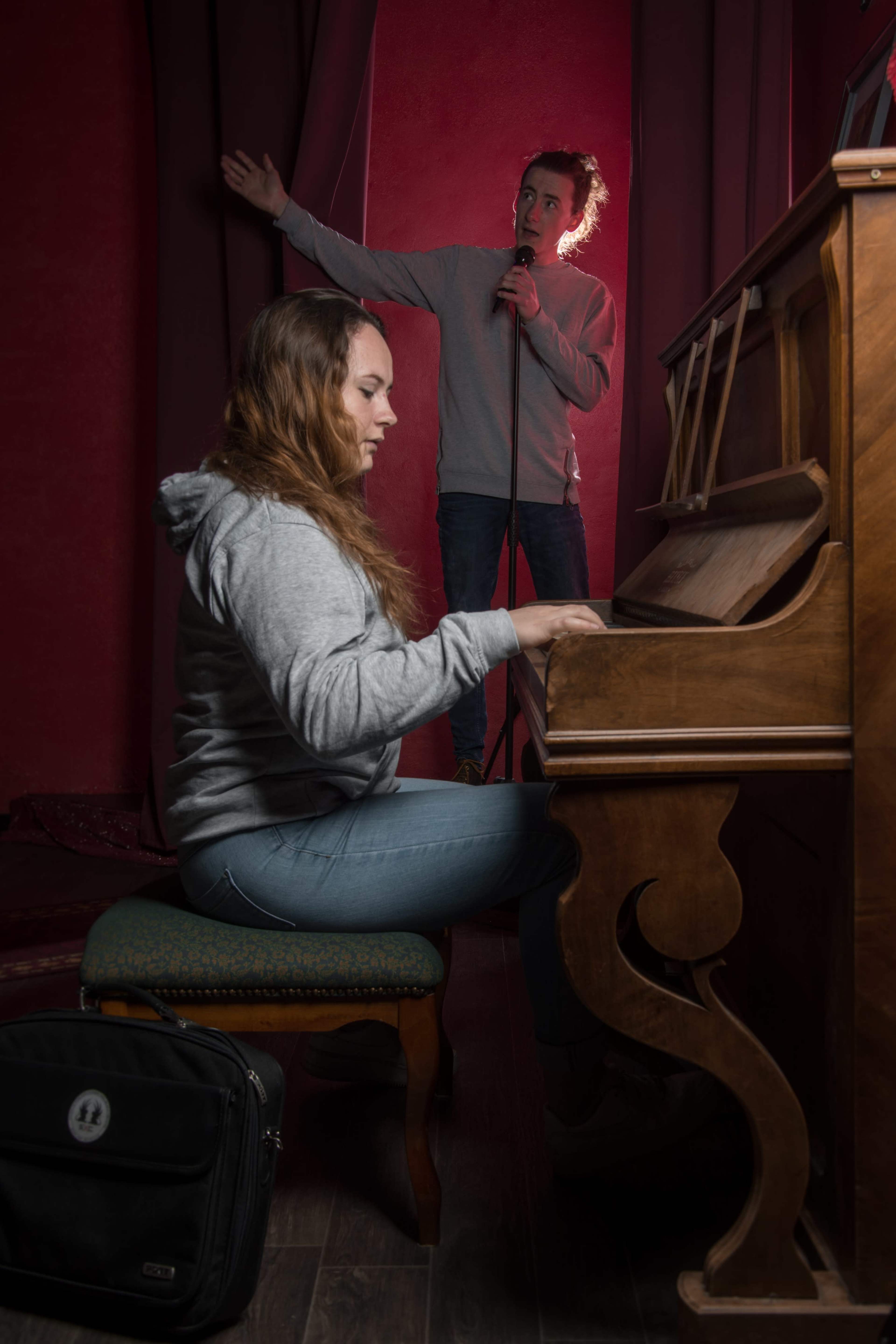 A woman plays a piano while a man stands behind her singing into a microphone.