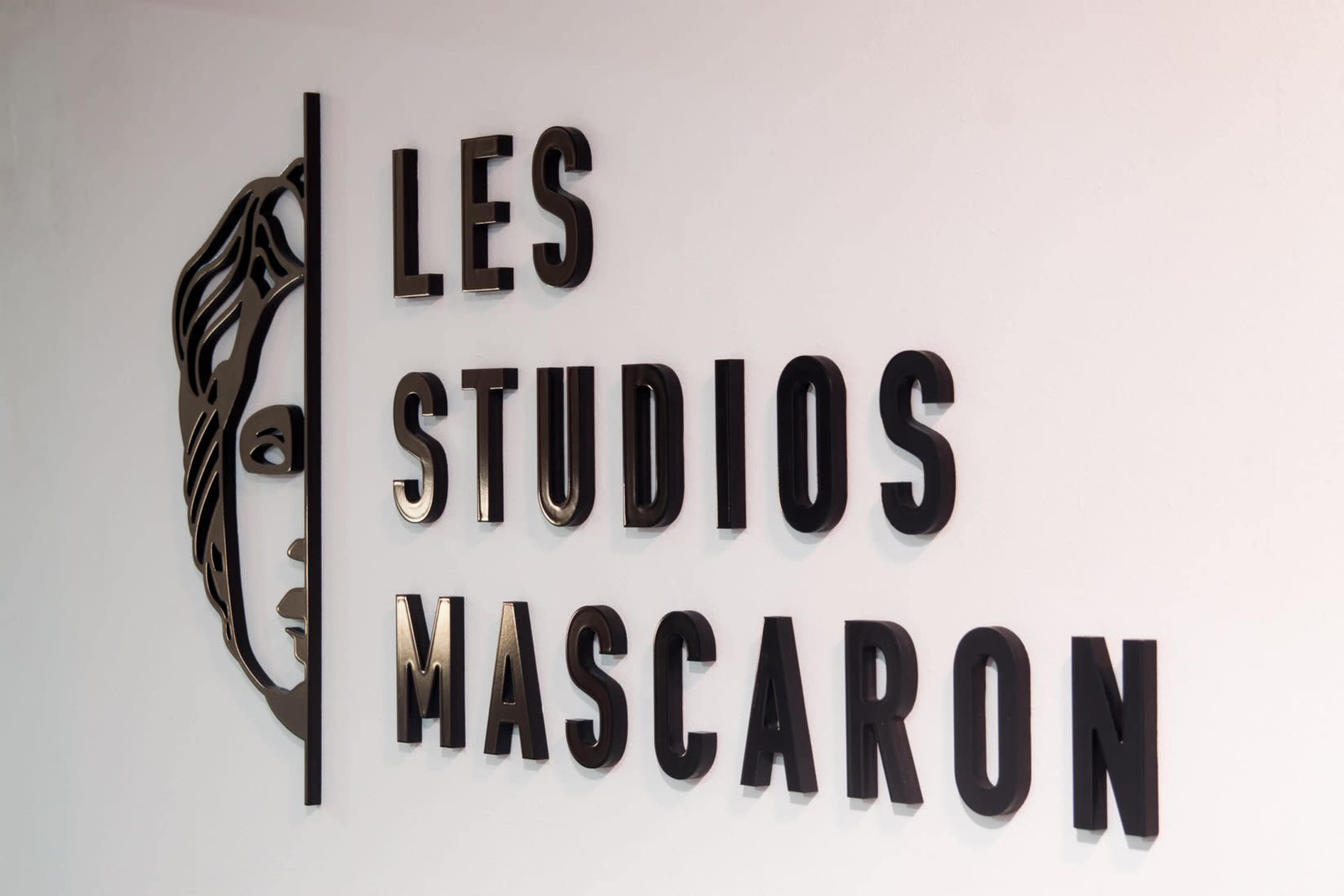 A wall sign displaying the text "LES STUDIOS MASCARON" alongside a stylized depiction of a face.