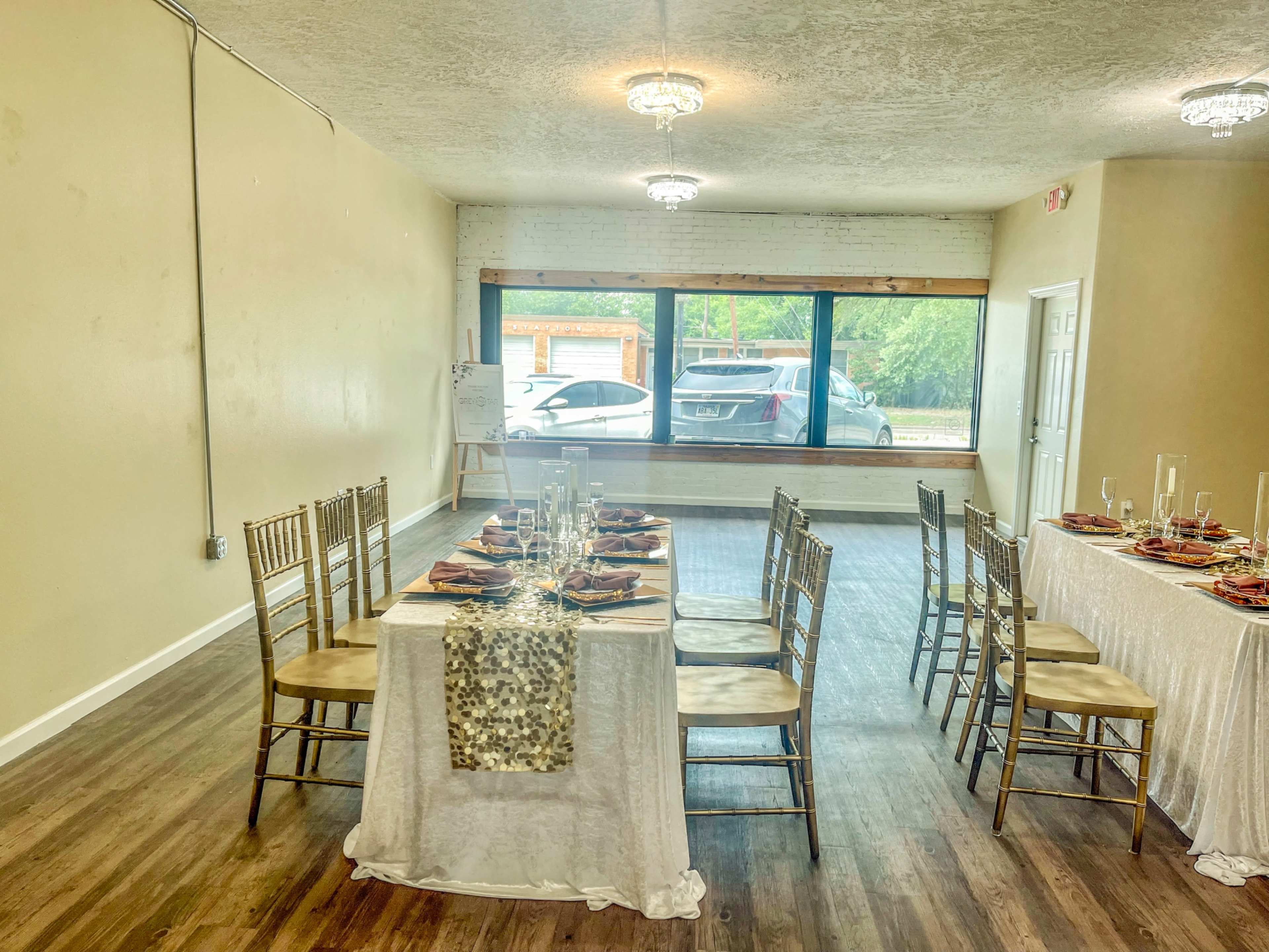 The room features two tables set for a dining arrangement, with elegant place settings and a large window overlooking a parking area.