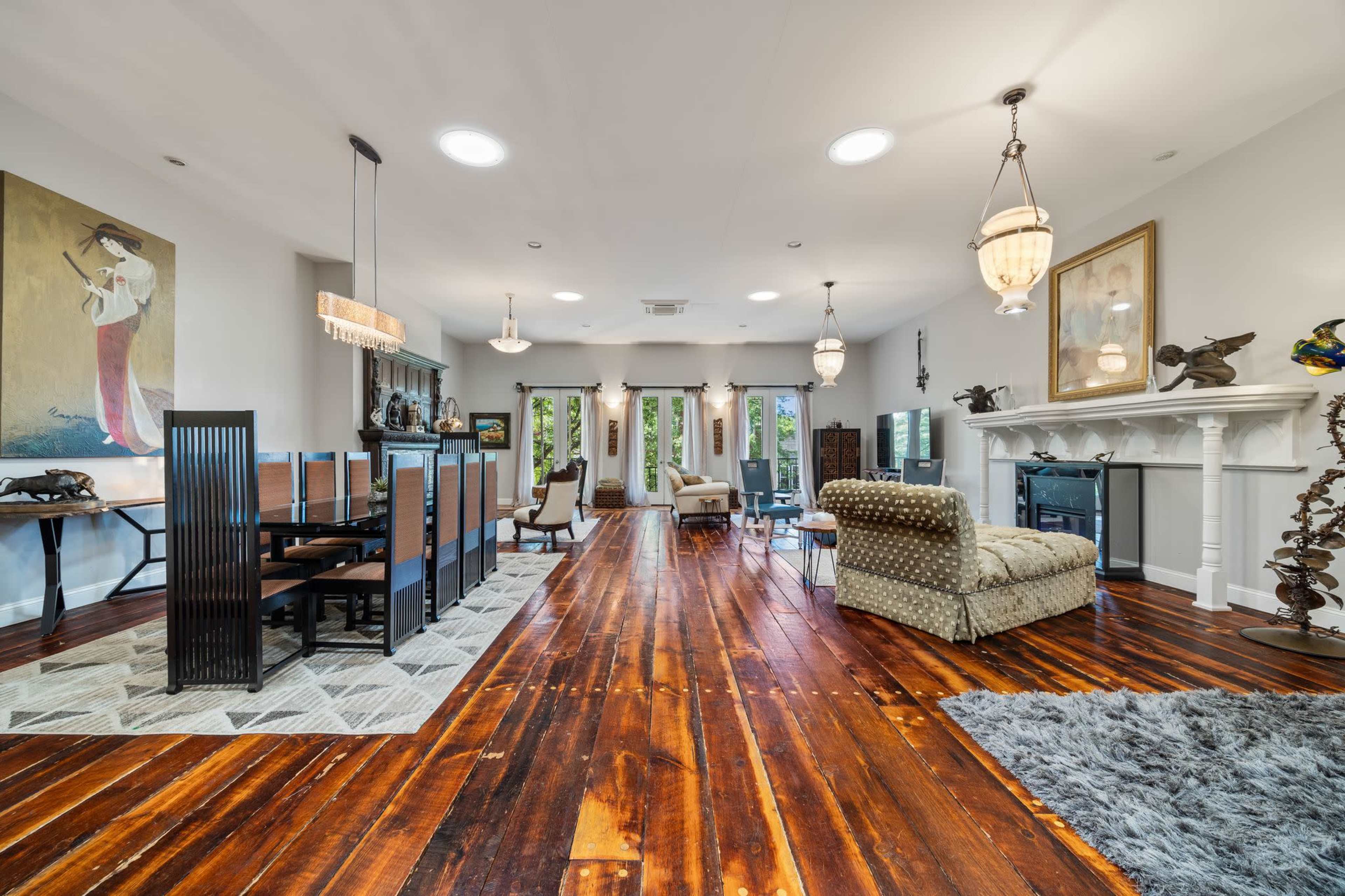 The image shows a spacious interior featuring a dining area with a long table and chairs, a living space with a couch and armchair, and hardwood floors with a large area rug.