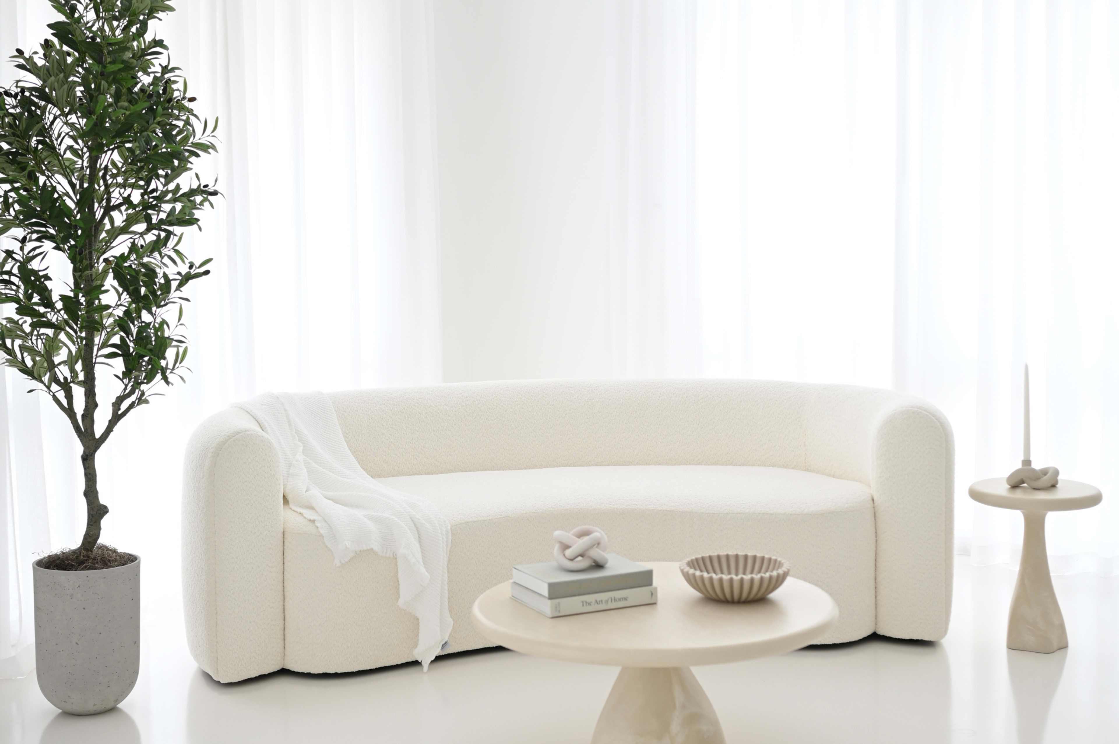 The scene features a modern, white upholstered couch beside a small round table with decor items and a plant in a gray pot.