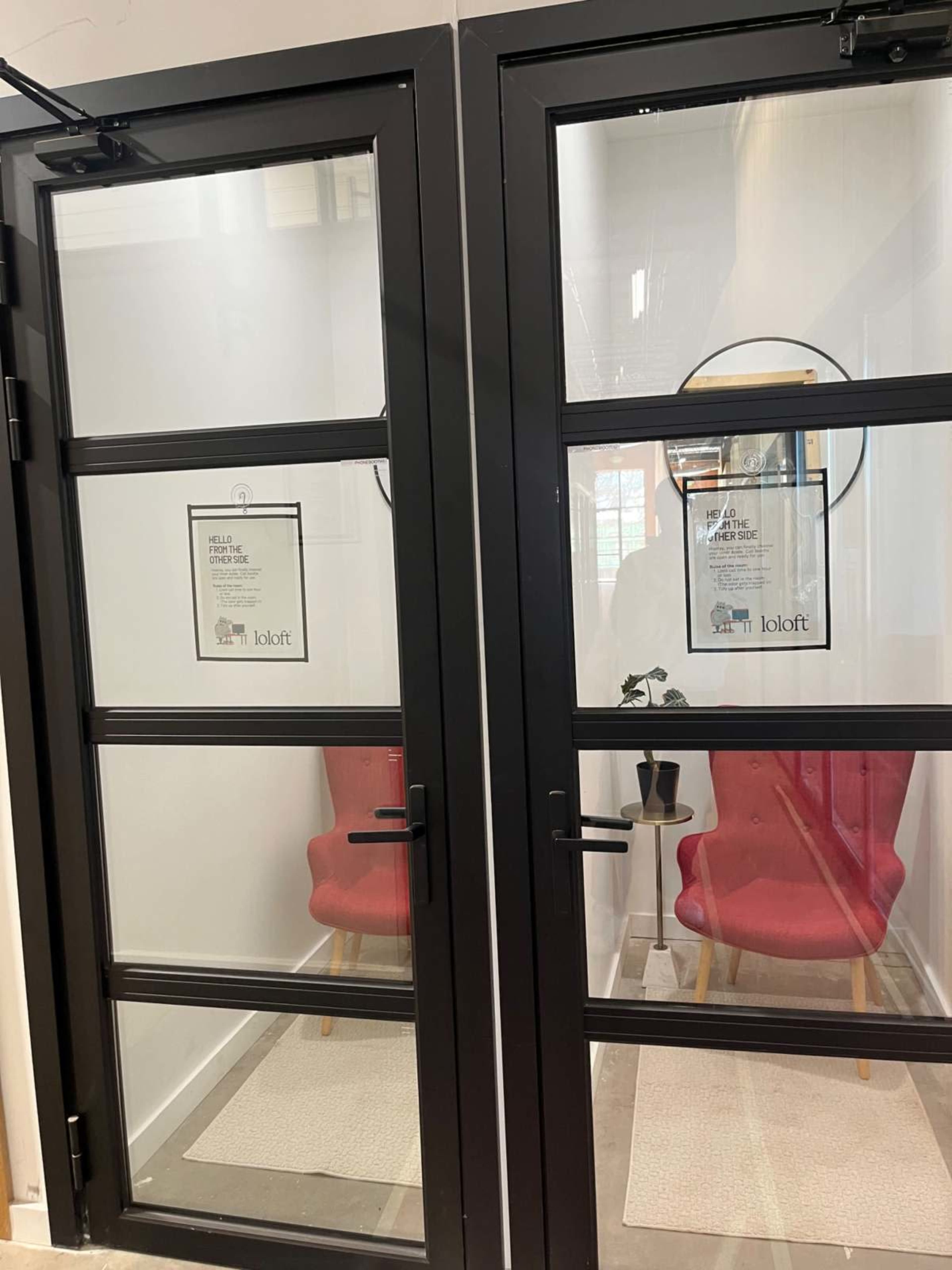 Two glass-paneled doors lead to a small waiting area with two pink chairs and a round mirror on the wall.