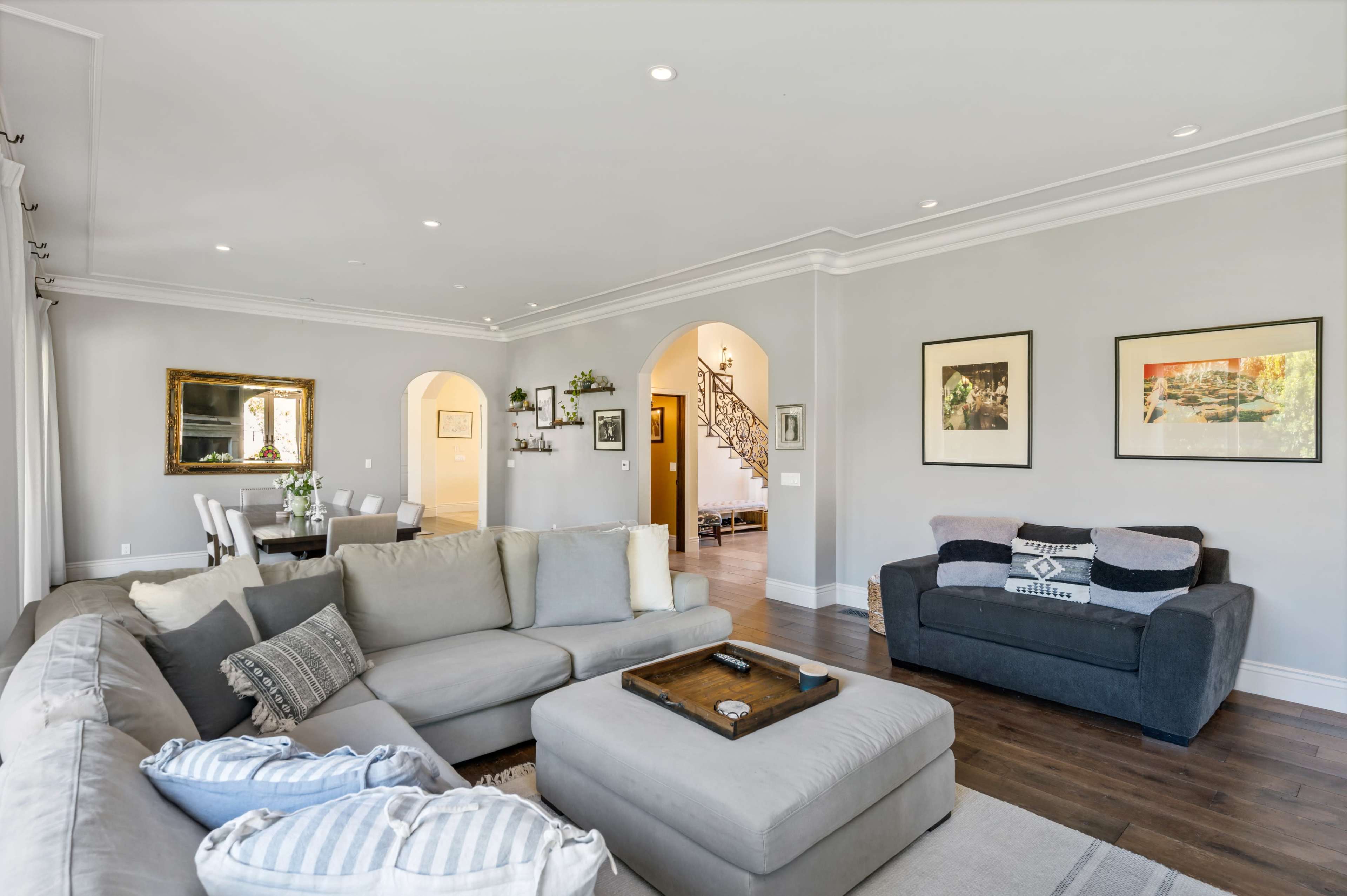 A modern living room with a large sectional couch, a coffee table, and arched doorways leading to a dining area and staircase.