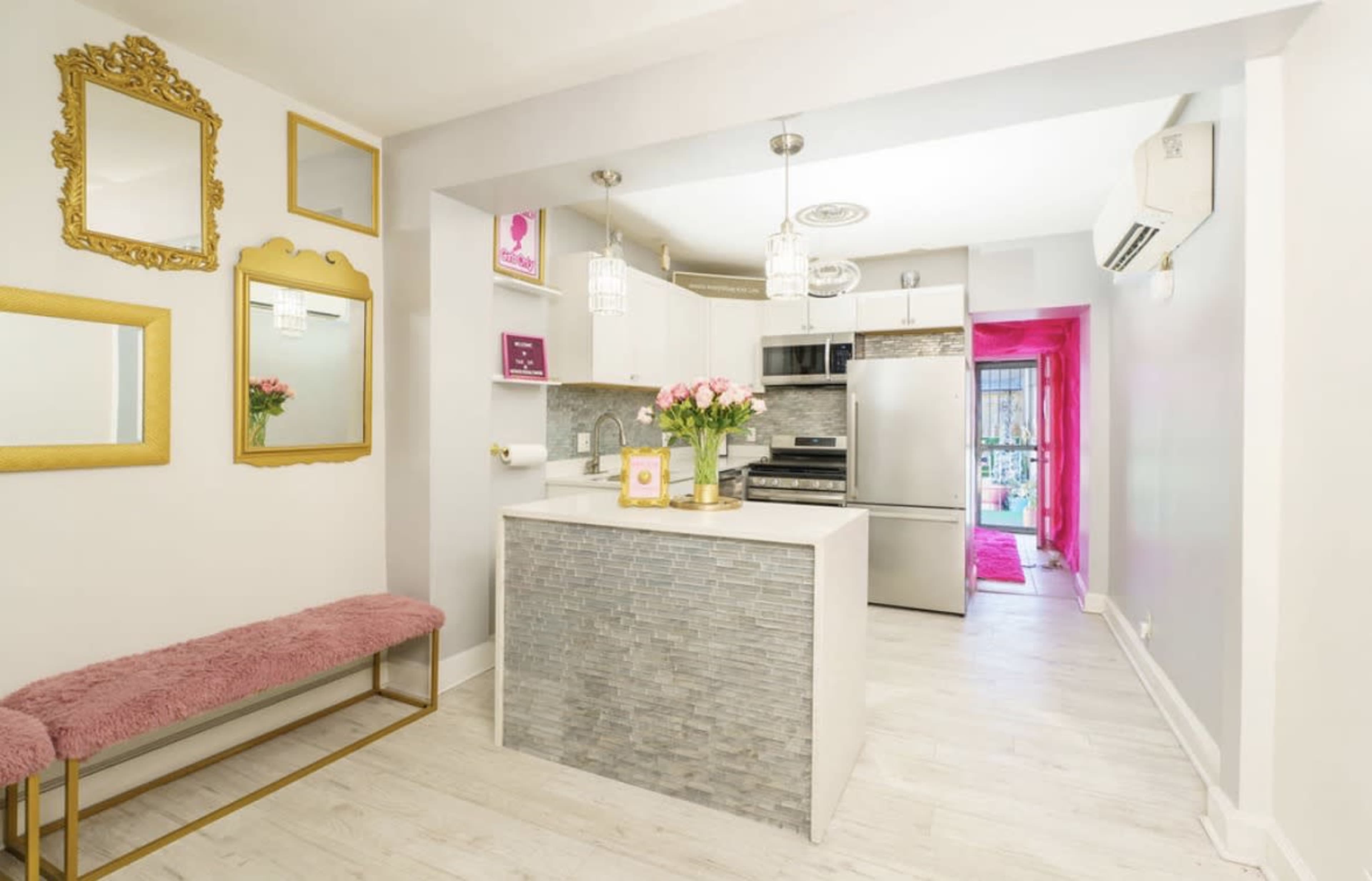 The image shows a modern kitchen area with a small bar, light-colored wooden floors, and decorative mirrors on the wall.