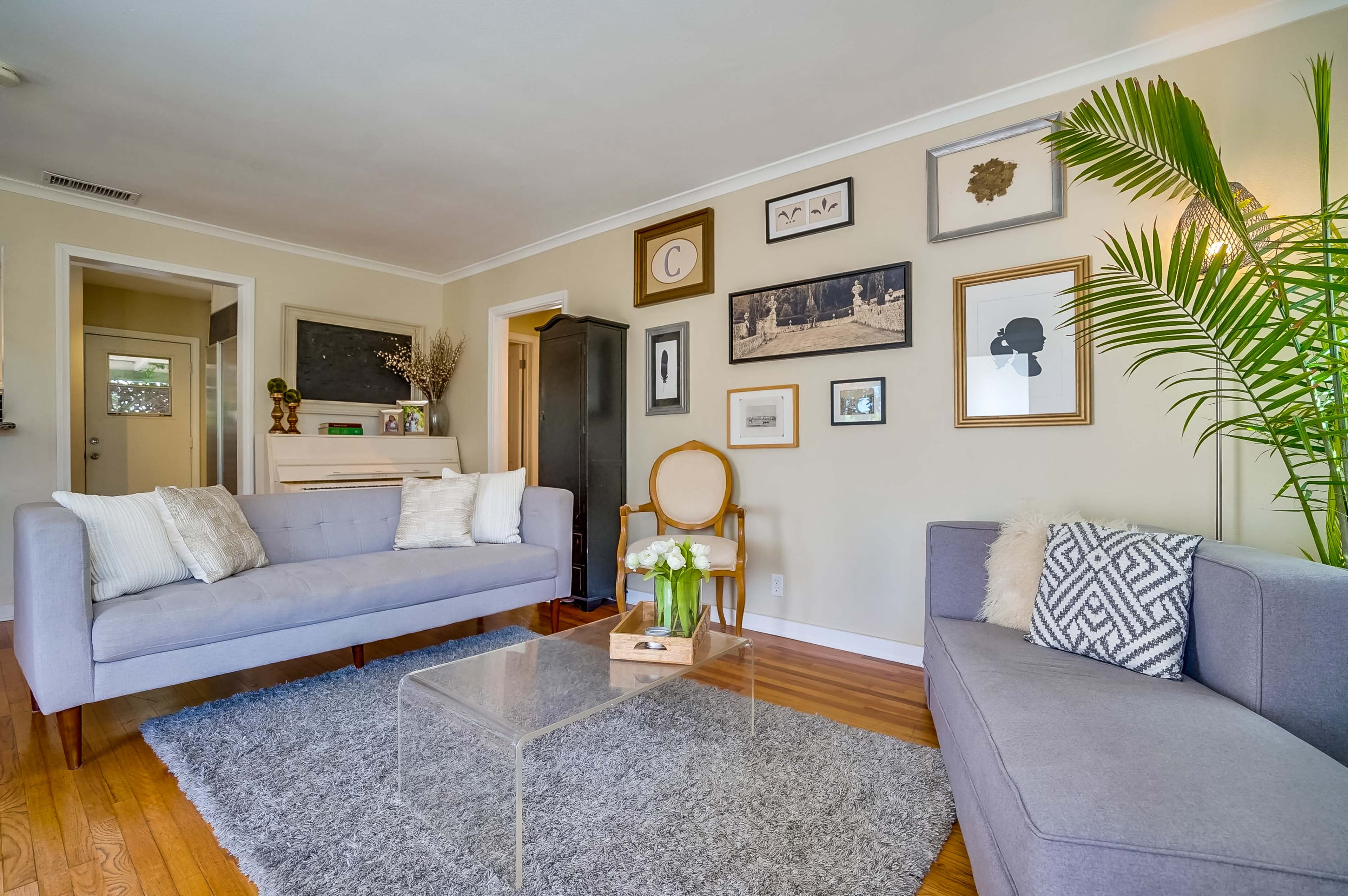 The living room features two sofas facing each other, a clear coffee table in the center, and a wall adorned with various framed artworks.