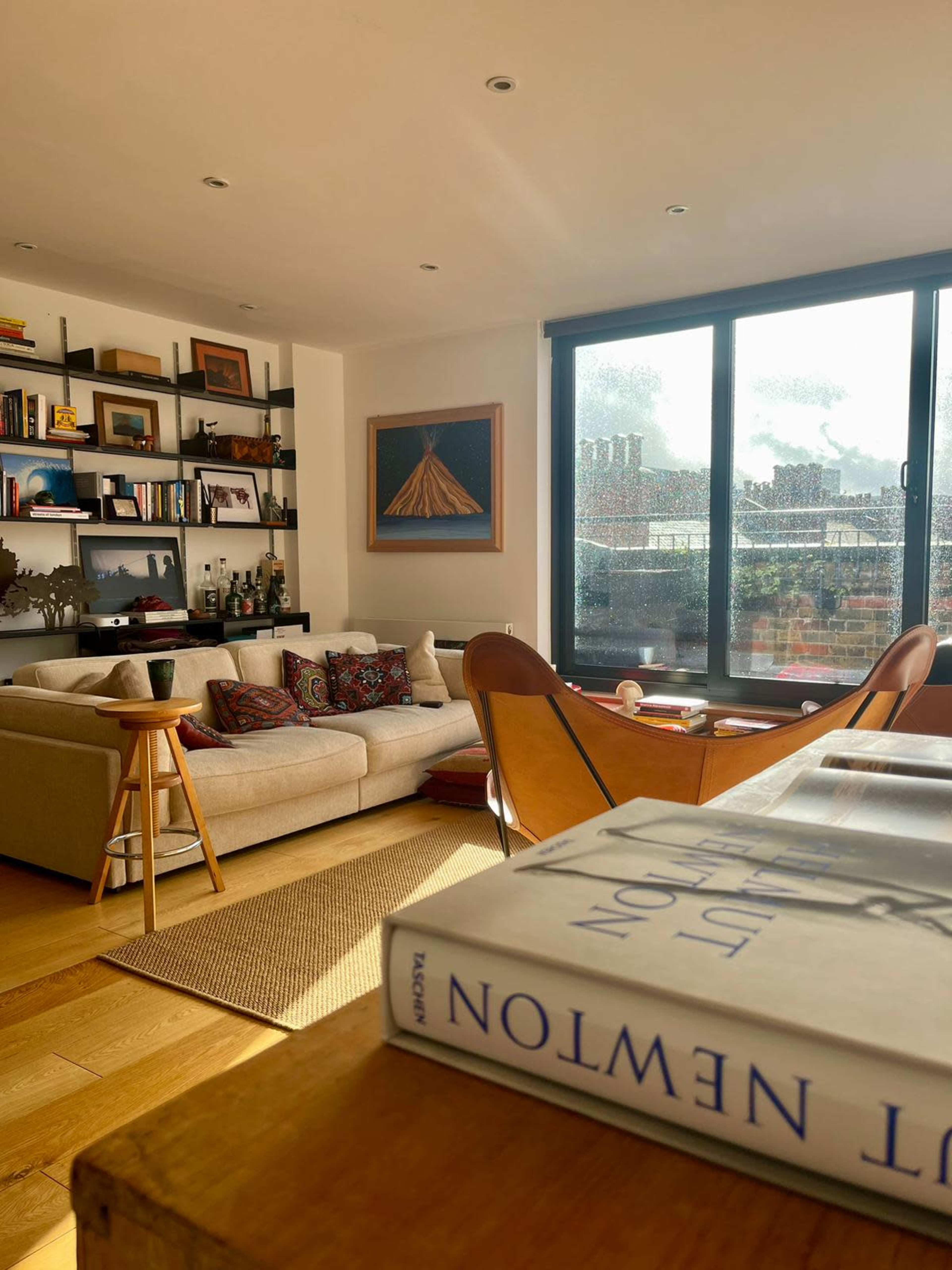 A cozy living room features a beige sofa, wooden shelves filled with books, and a coffee table with a book lying open.