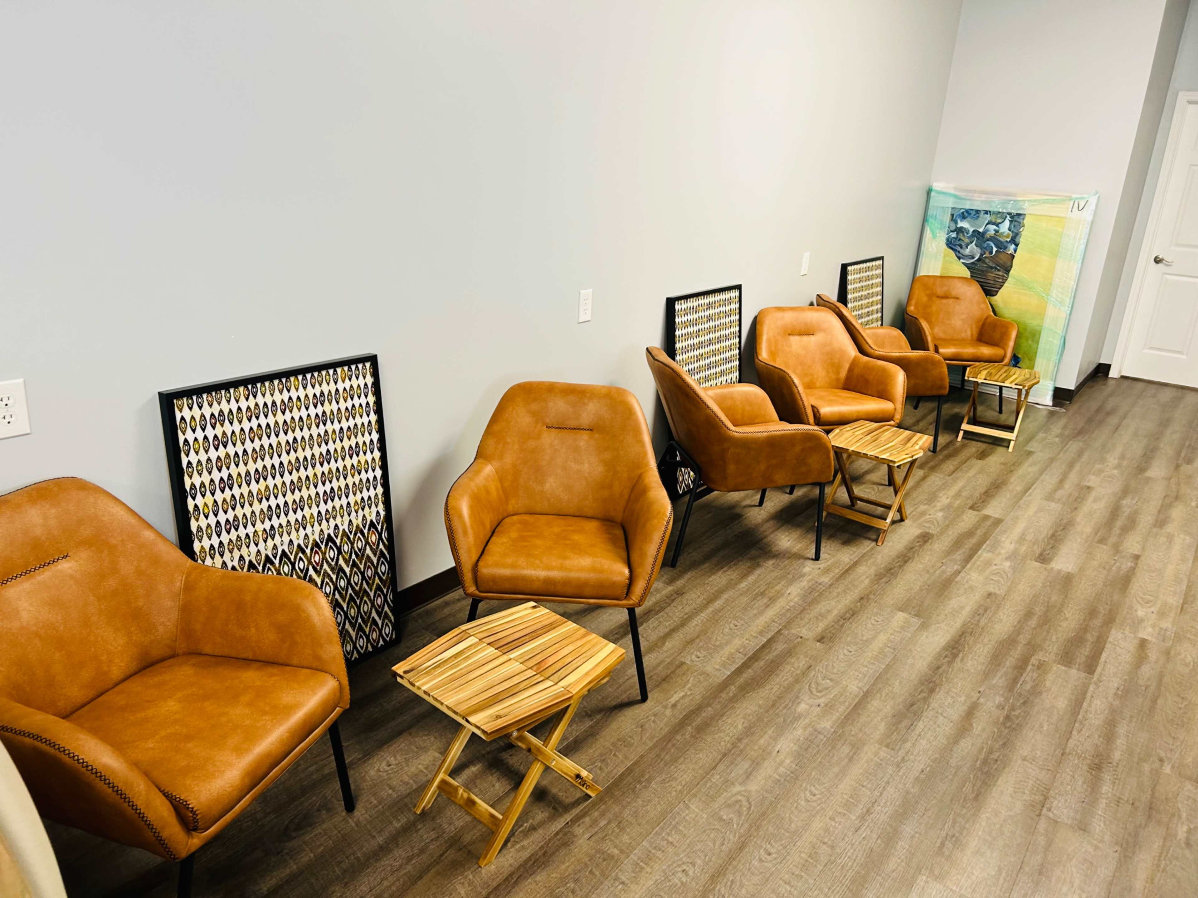 A waiting area with five brown leather chairs arranged around a small wooden table against a gray wall.