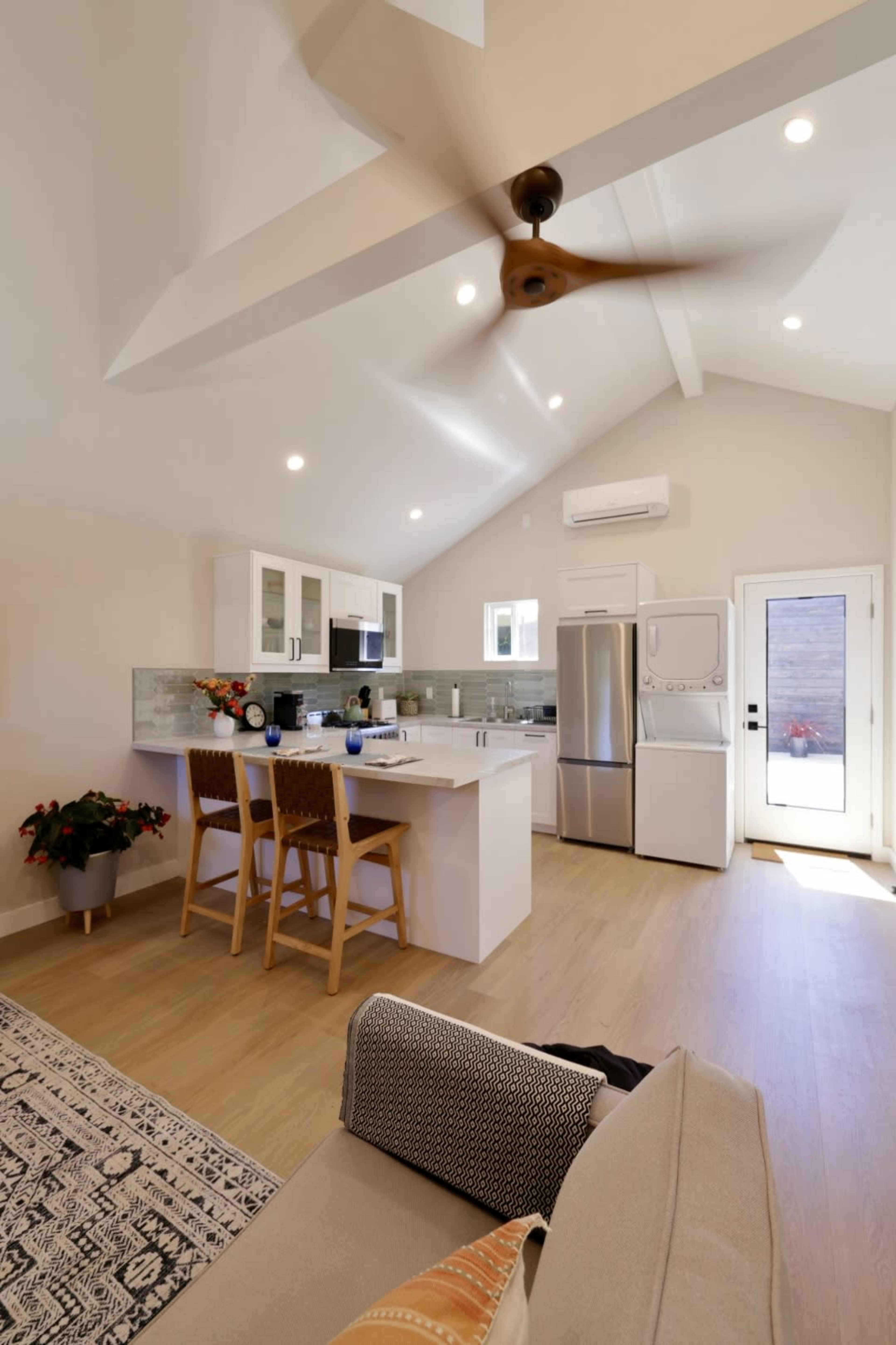 A modern kitchen with a central island, bar stools, stainless steel appliances, and a sliding glass door leading to an outdoor area.