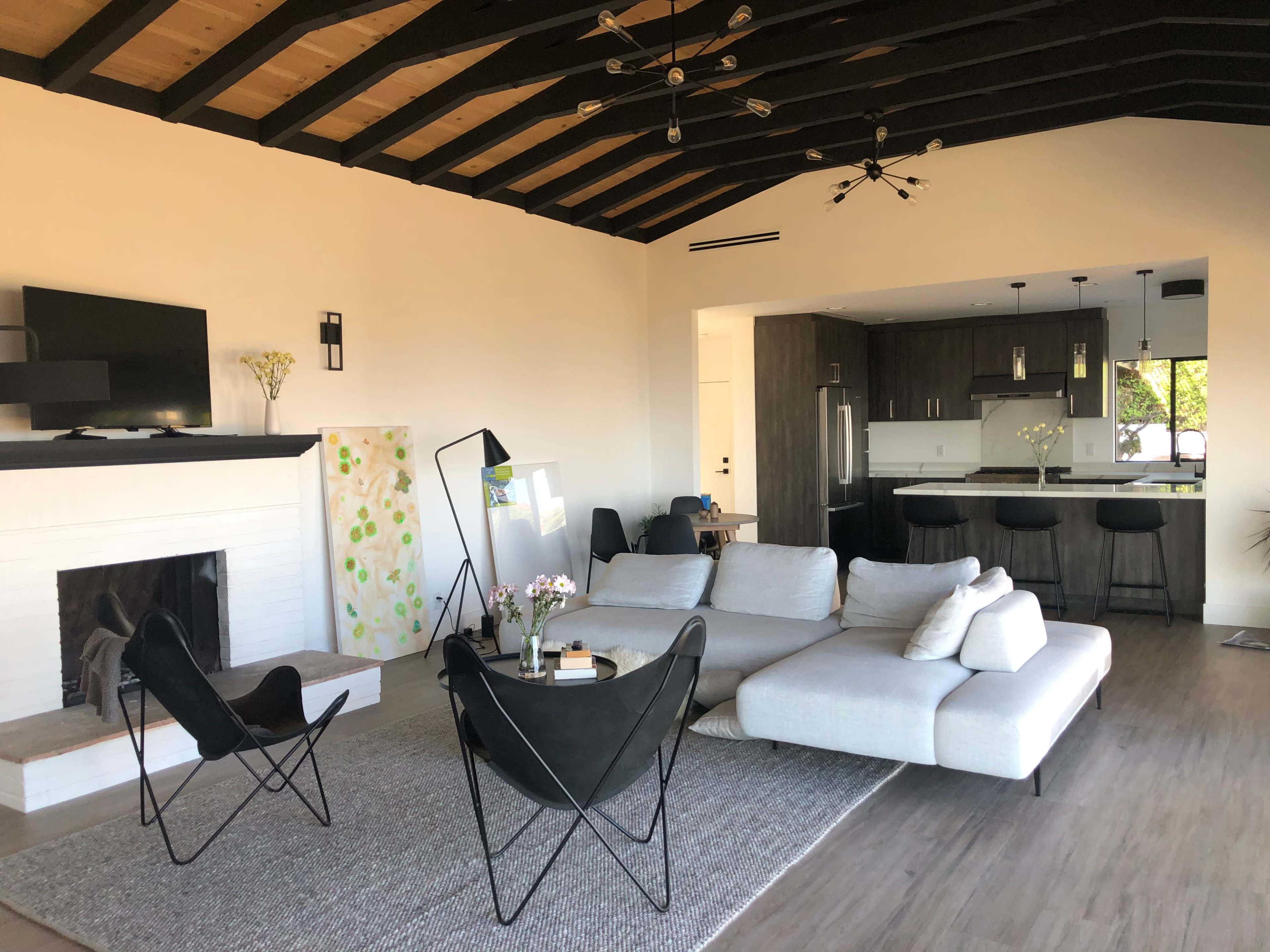 A modern living room with a sectional sofa, a black chair, a coffee table, a fireplace, and an open kitchen in the background.