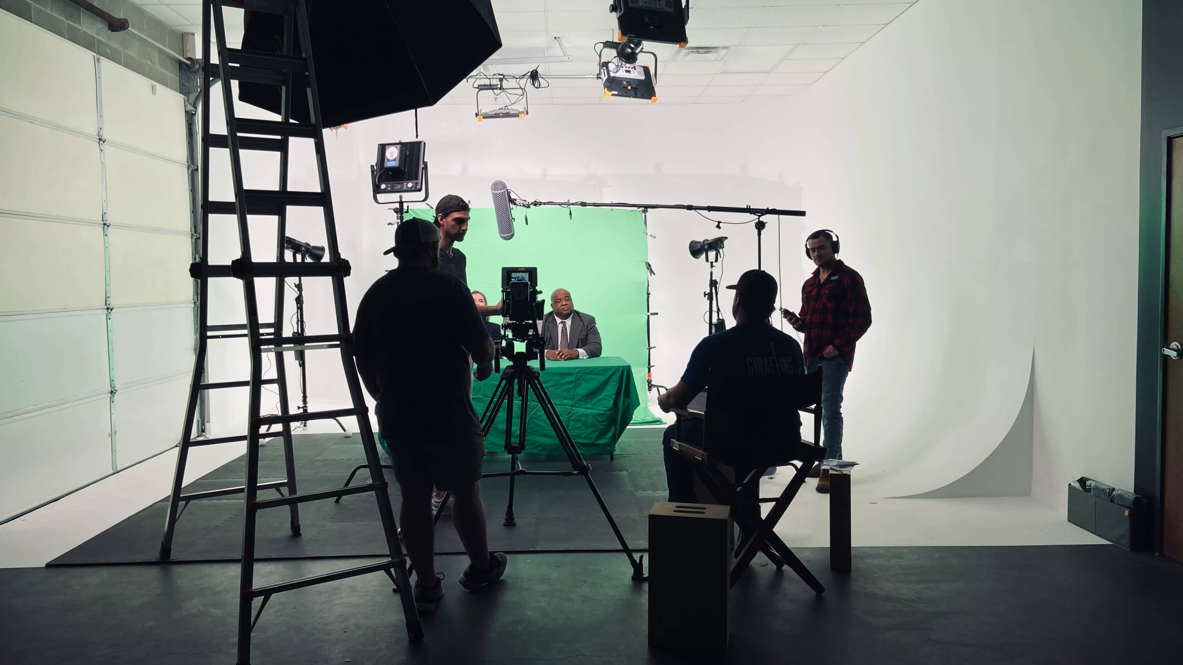 A film crew sets up for a recording session in a studio with a green screen backdrop.