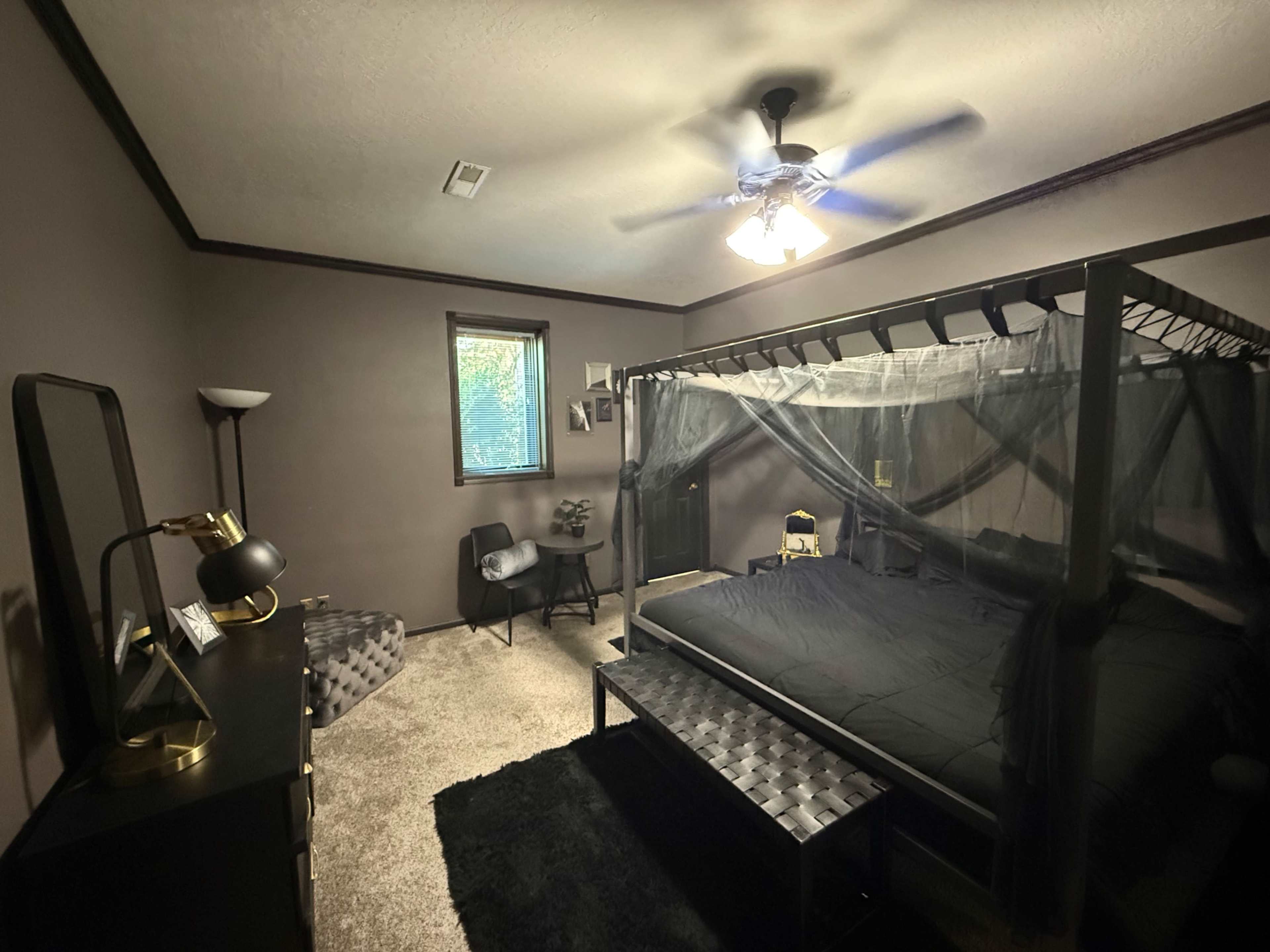 The bedroom features a canopy bed with a sheer curtain, a sitting area with a chair and lamp, and a dark color scheme.