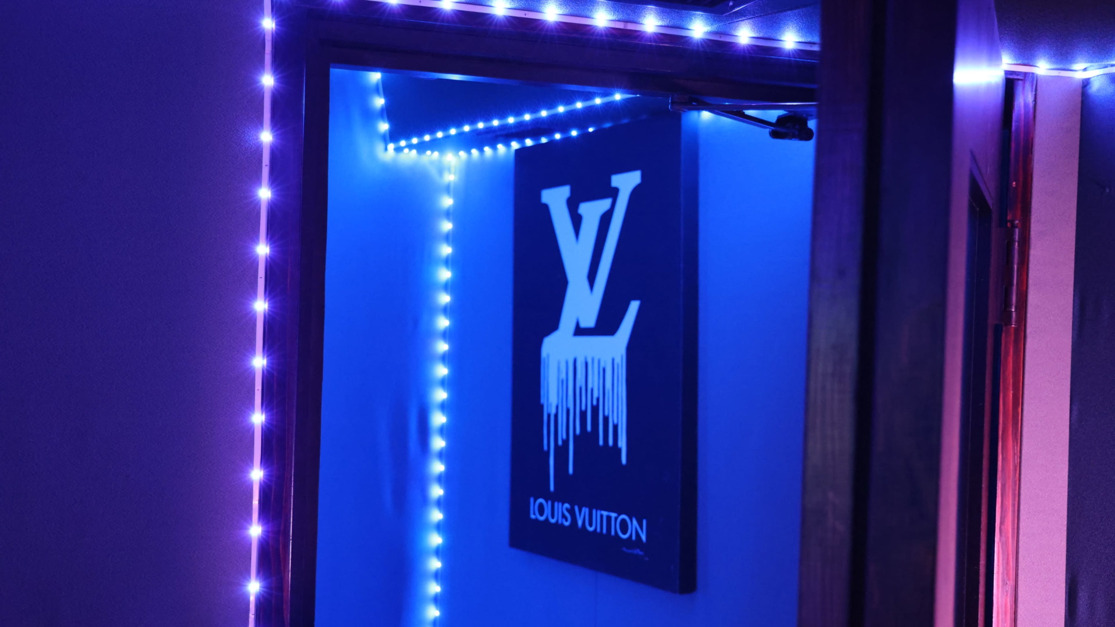 A room entrance with blue LED lights framing a wall displaying a Louis Vuitton logo.
