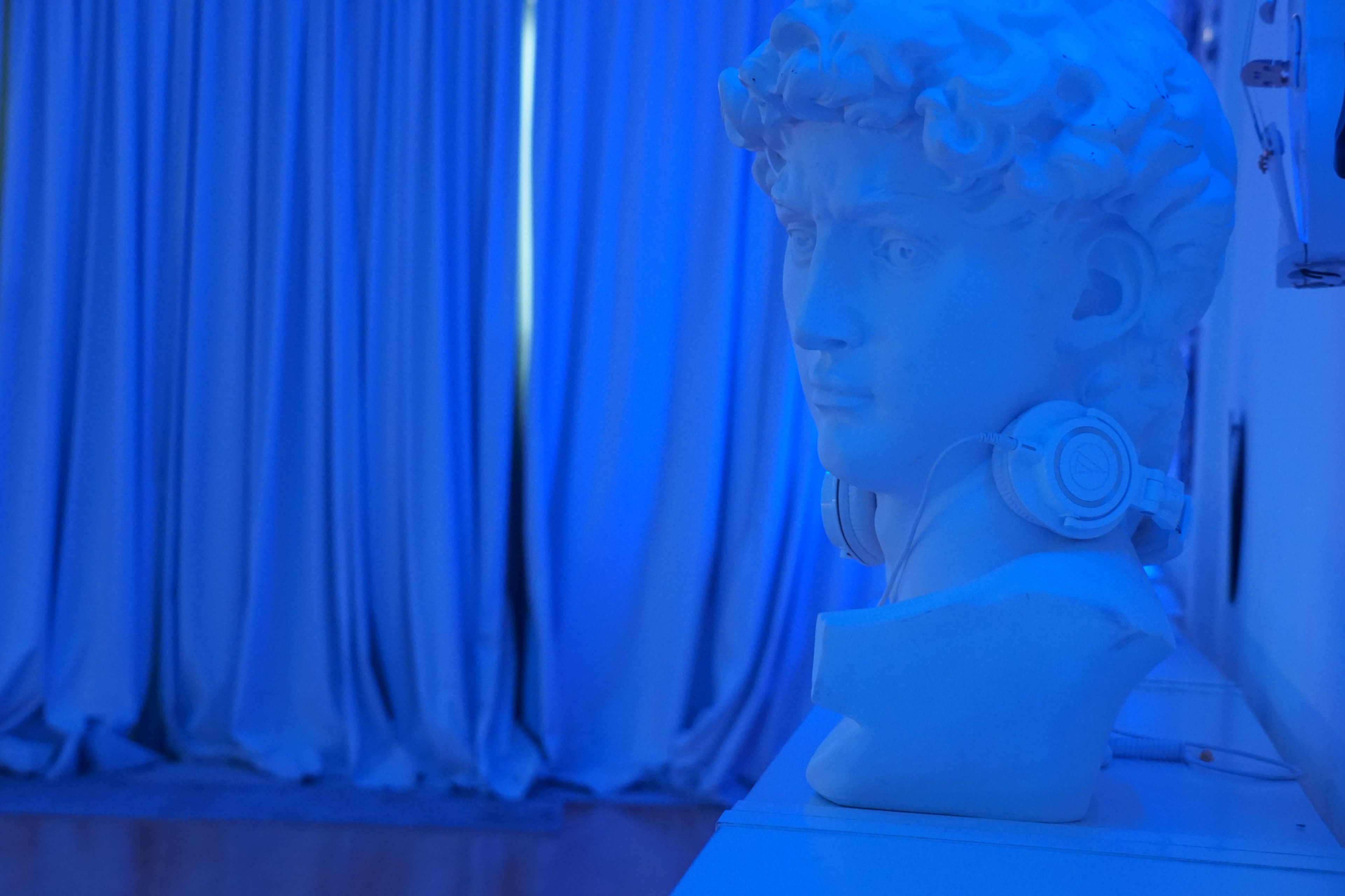 A white bust of a man with headphones rests on a shelf in a room illuminated with blue light.
