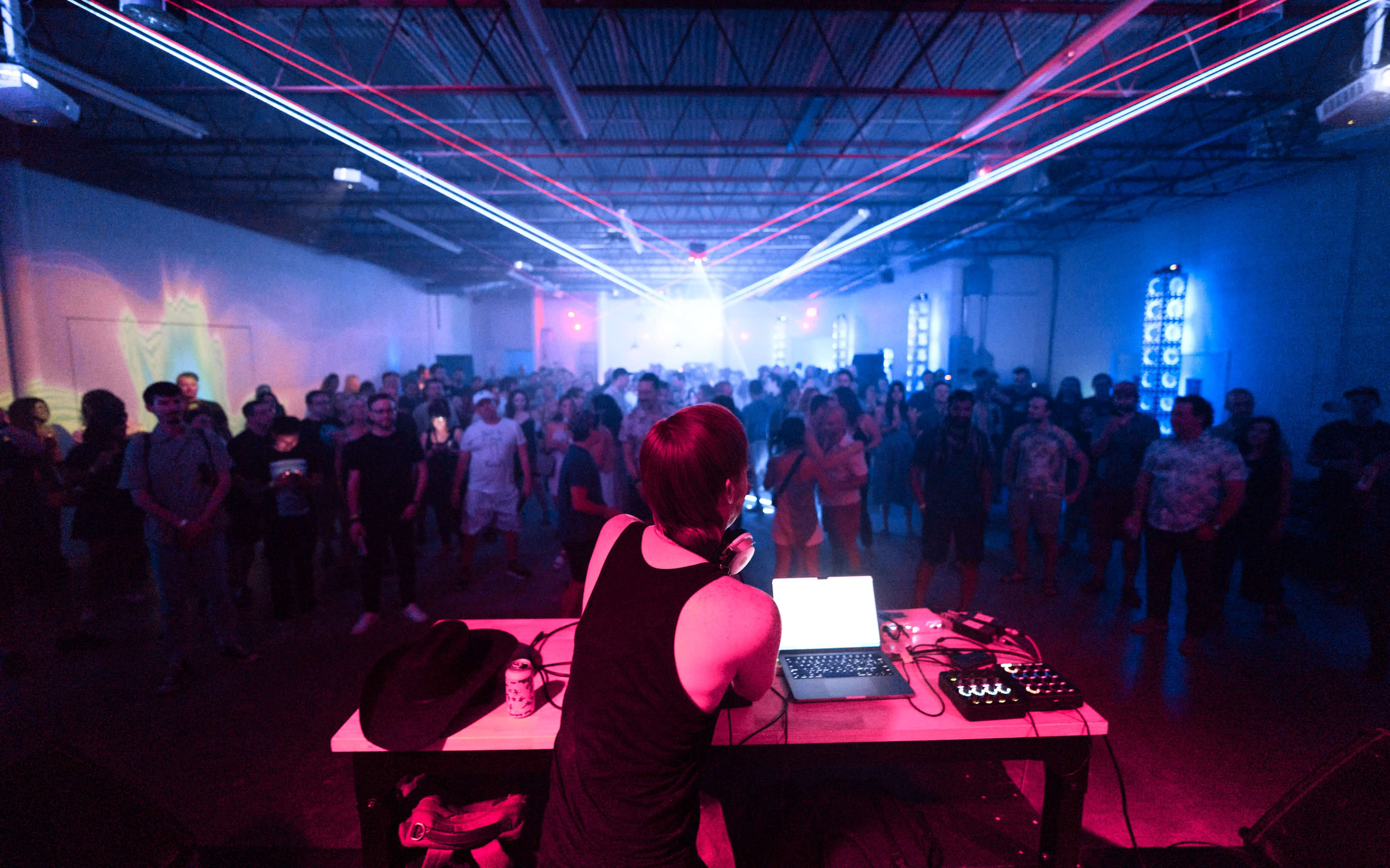 A DJ performs on stage in front of an audience, with vibrant lasers illuminating the space around them.