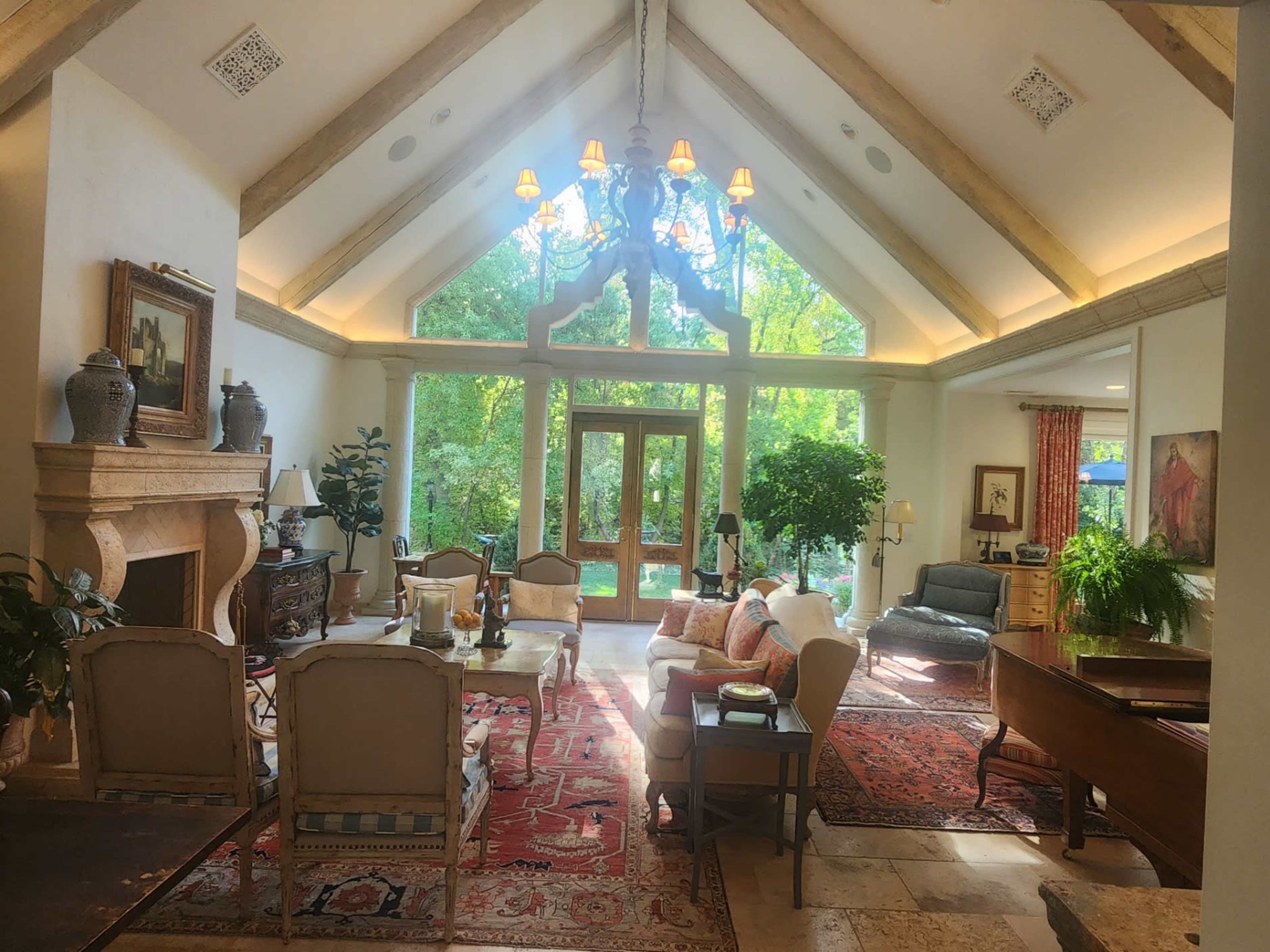 The image shows a spacious living room with high, vaulted ceilings, large windows providing natural light, and a mix of elegant seating arrangements.