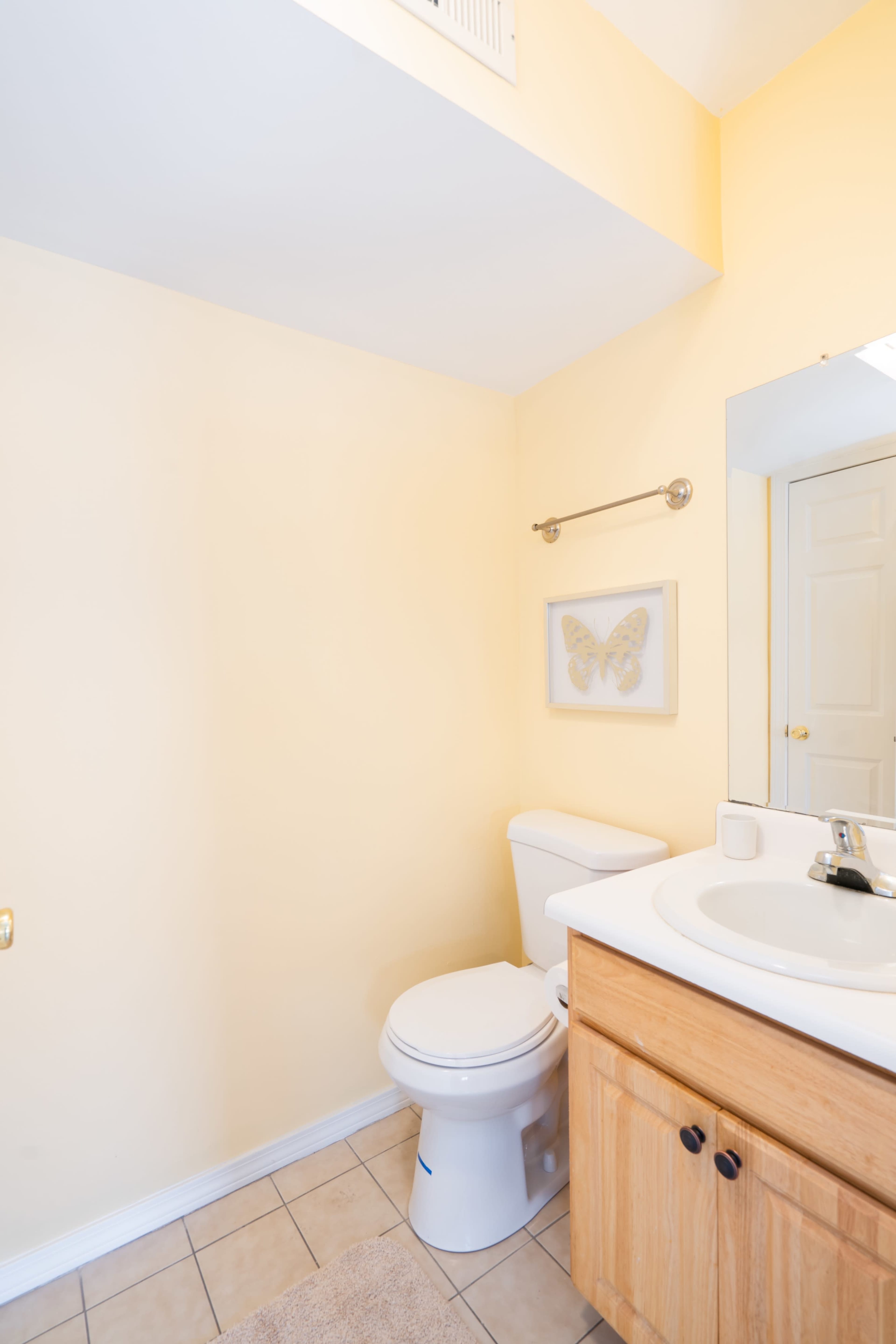 A small bathroom with yellow walls, a toilet, a sink with a wooden cabinet, and a framed butterfly decoration on the wall.