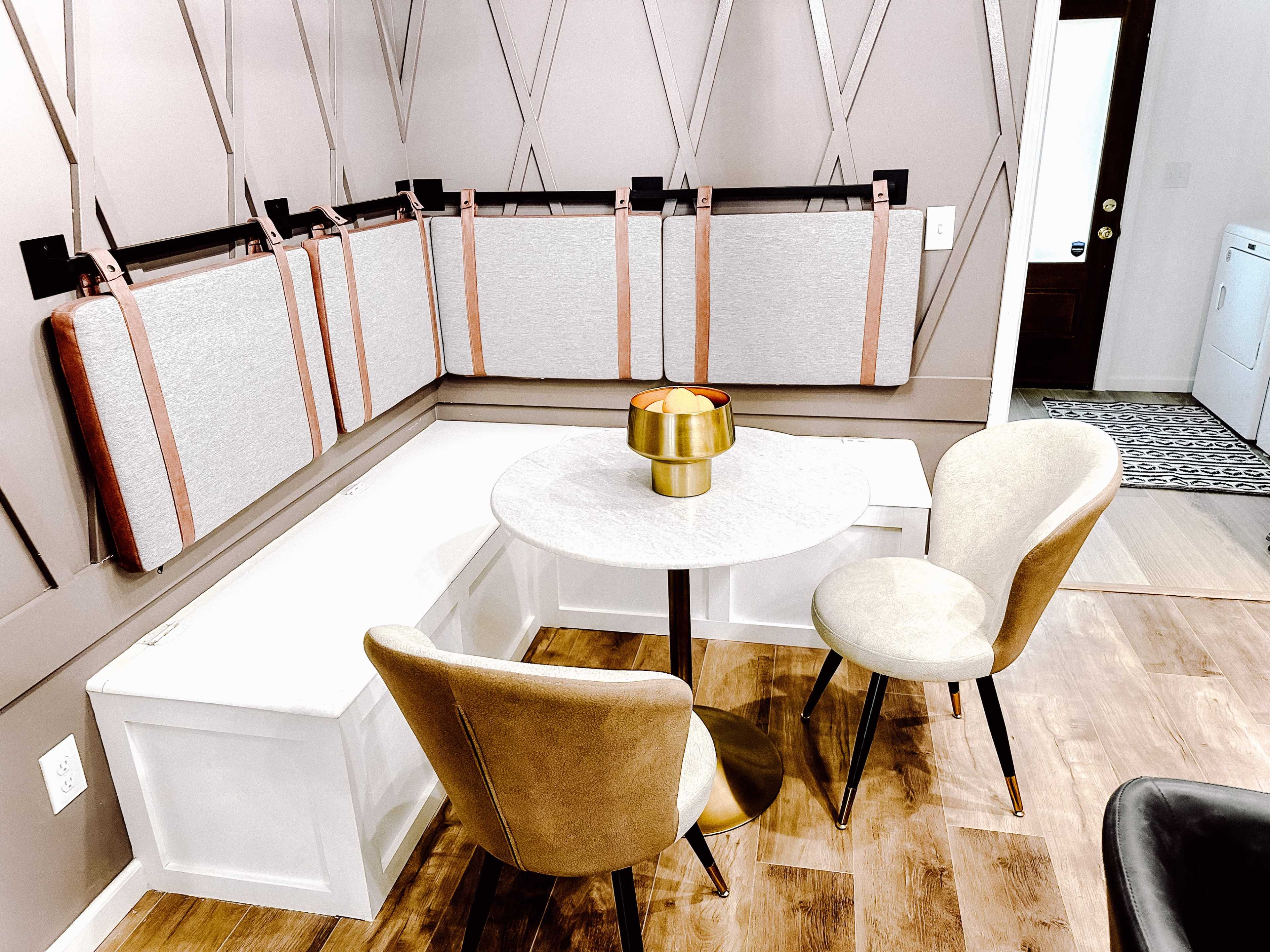 A small dining area with a round table, two upholstered chairs, and a built-in bench with decorative cushions against the wall.