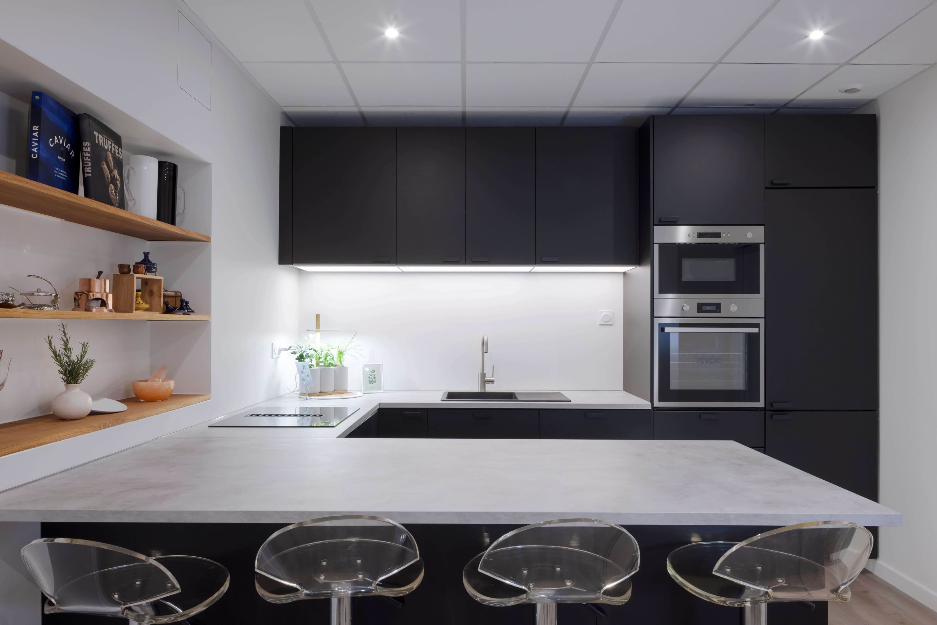 A modern kitchen with black cabinetry, a white countertop, and three transparent stools at a kitchen island.