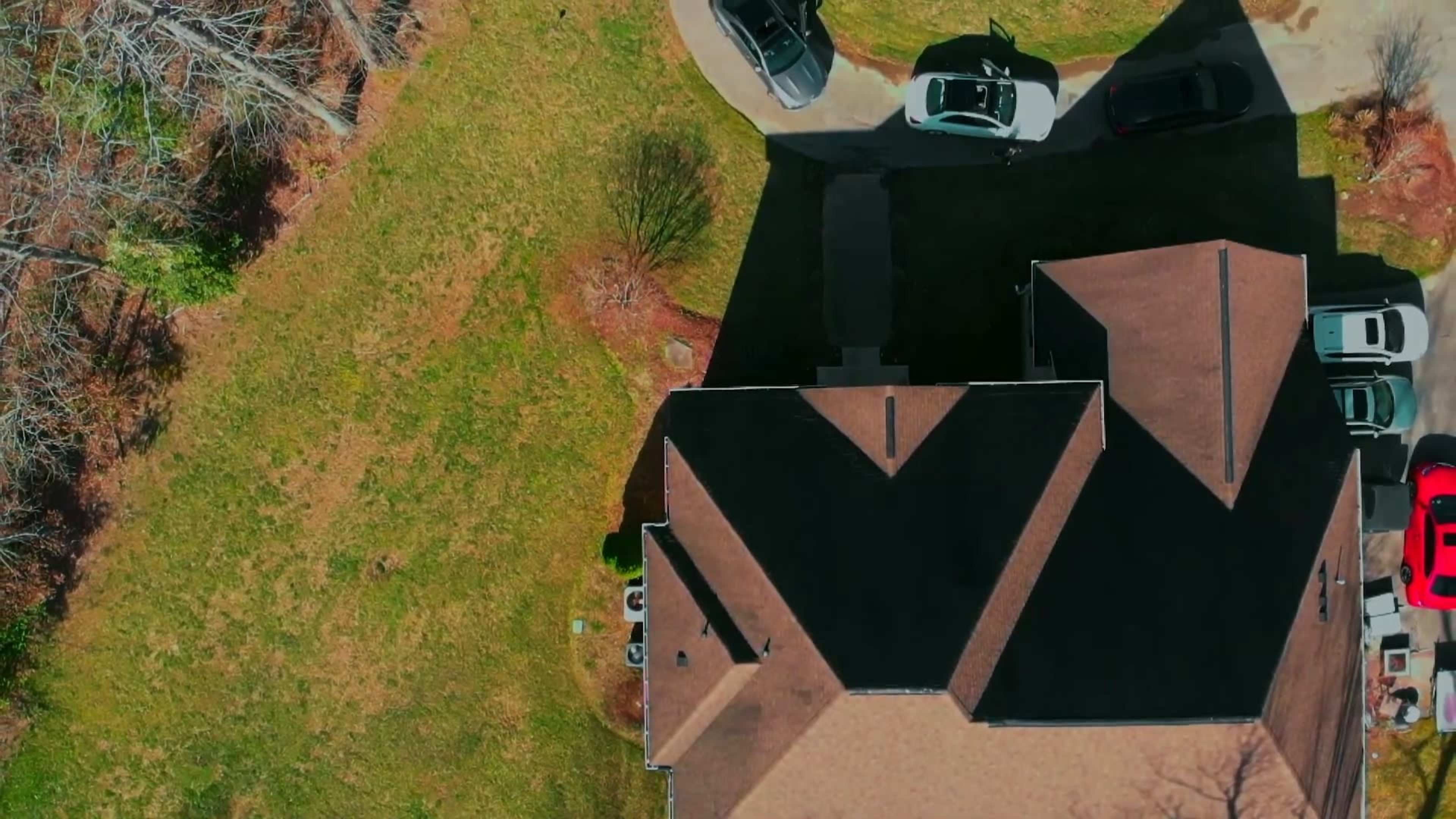 An aerial view of a residential property with several cars parked in a driveway and a large expanse of grass surrounding the house.