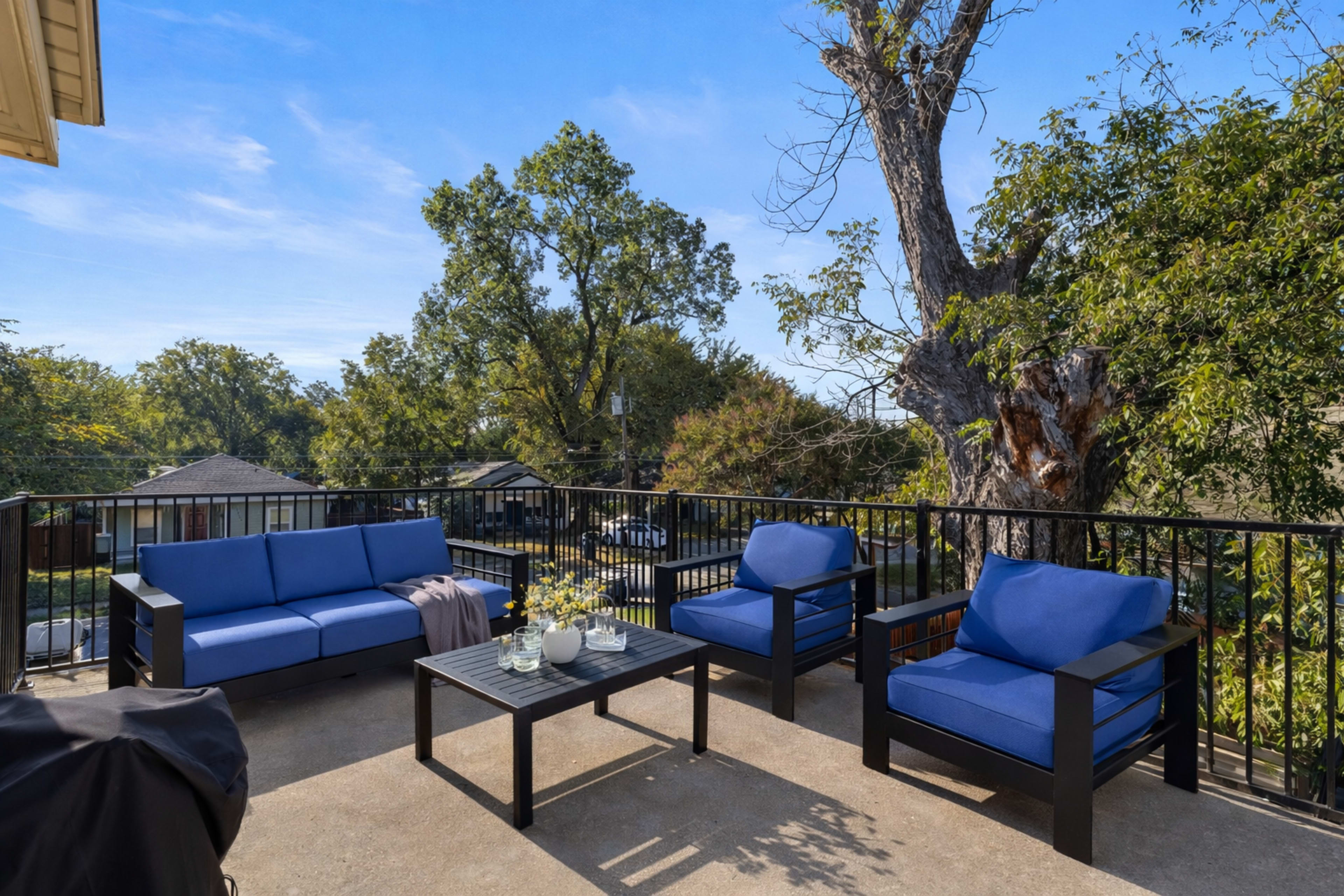 A patio area features blue outdoor furniture, including a sofa and chairs, arranged around a coffee table, with trees and houses visible in the background.