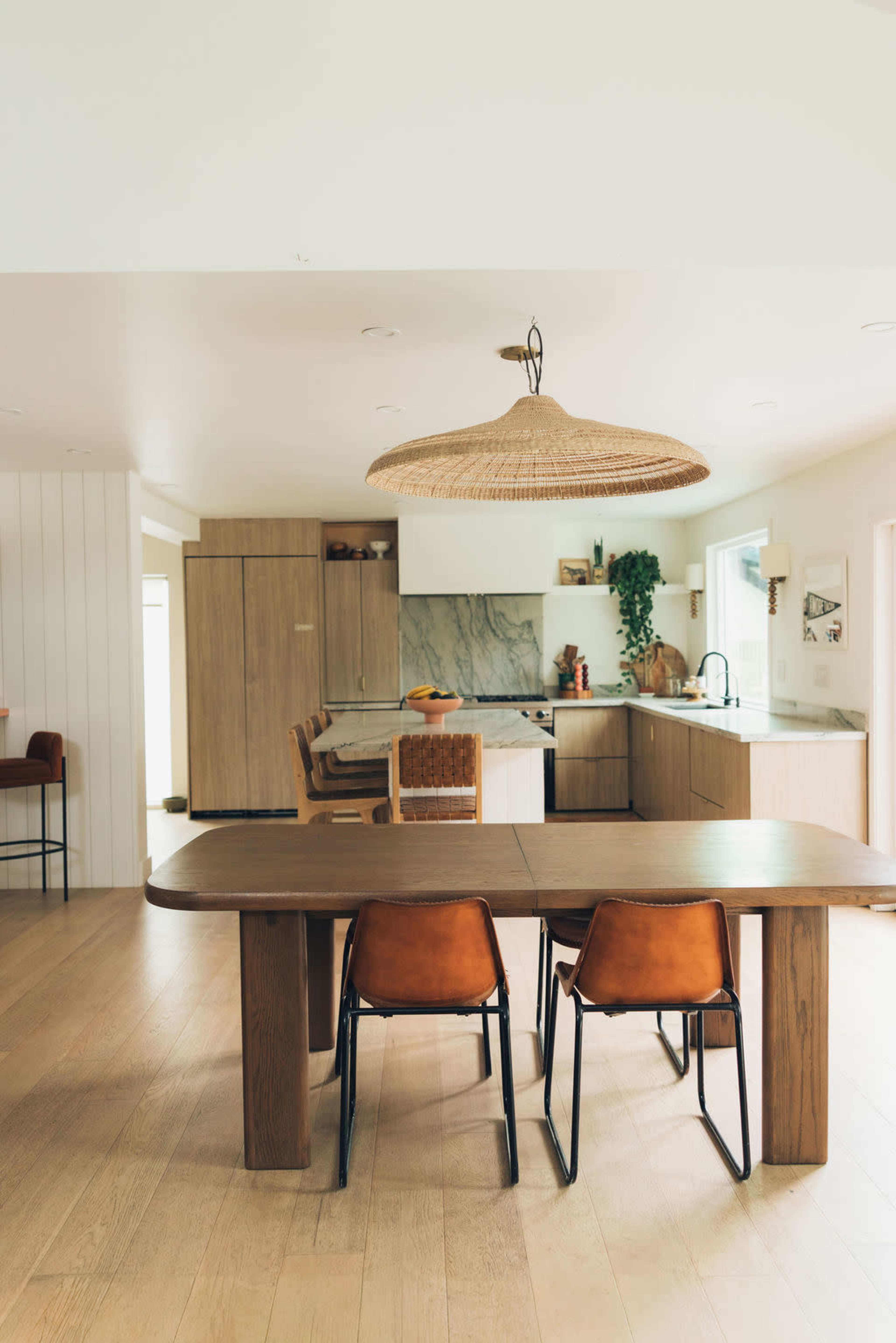 A spacious kitchen features a large wooden table with two leather chairs, surrounded by cabinets and a marble countertop.