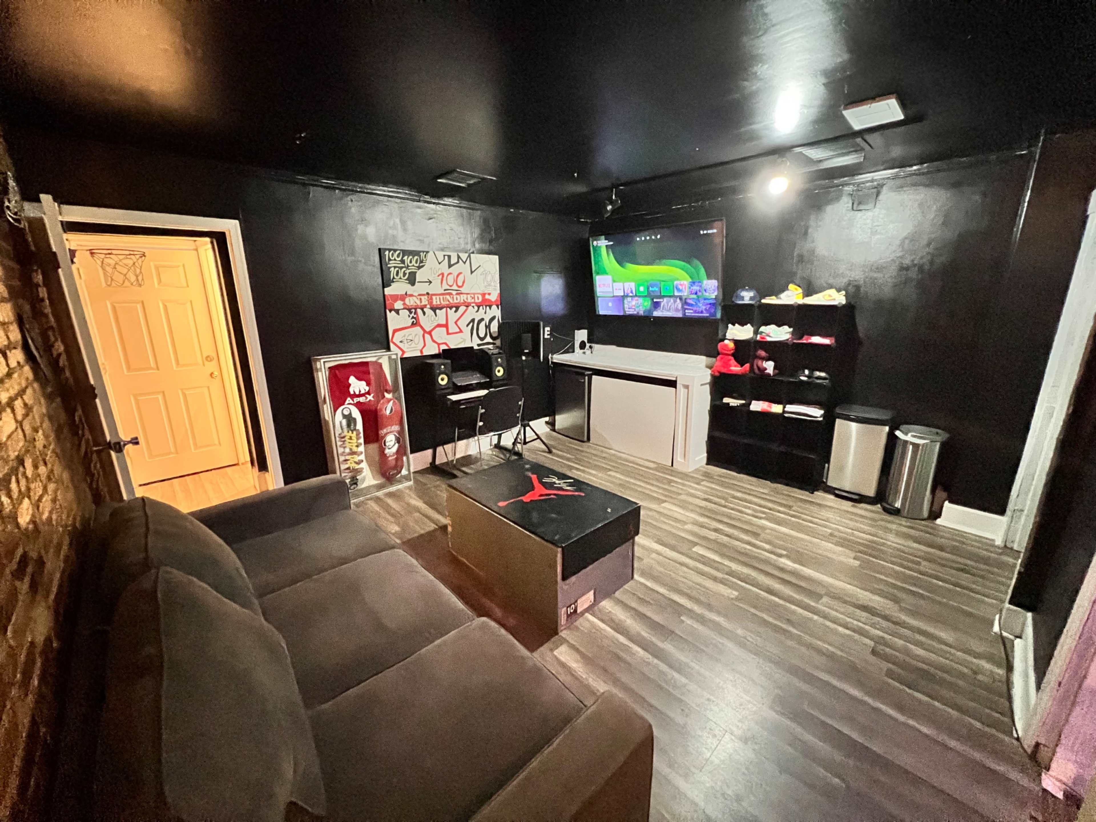 A small room features a dark-colored couch, a coffee table with a graphic design, audio equipment, and shelves displaying shoes and accessories.