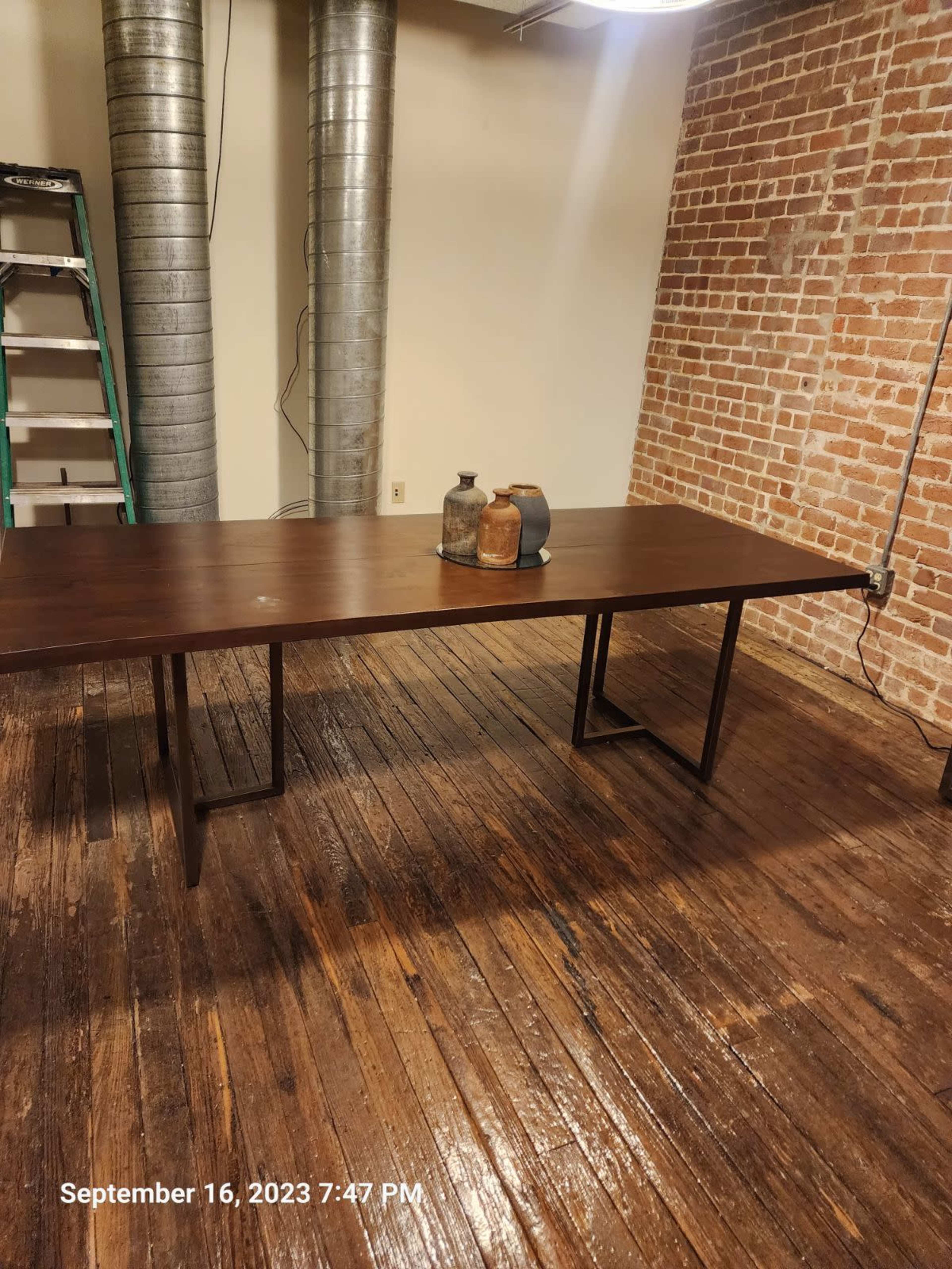 A wooden table is positioned in a room with exposed brick walls and industrial-style ductwork overhead.