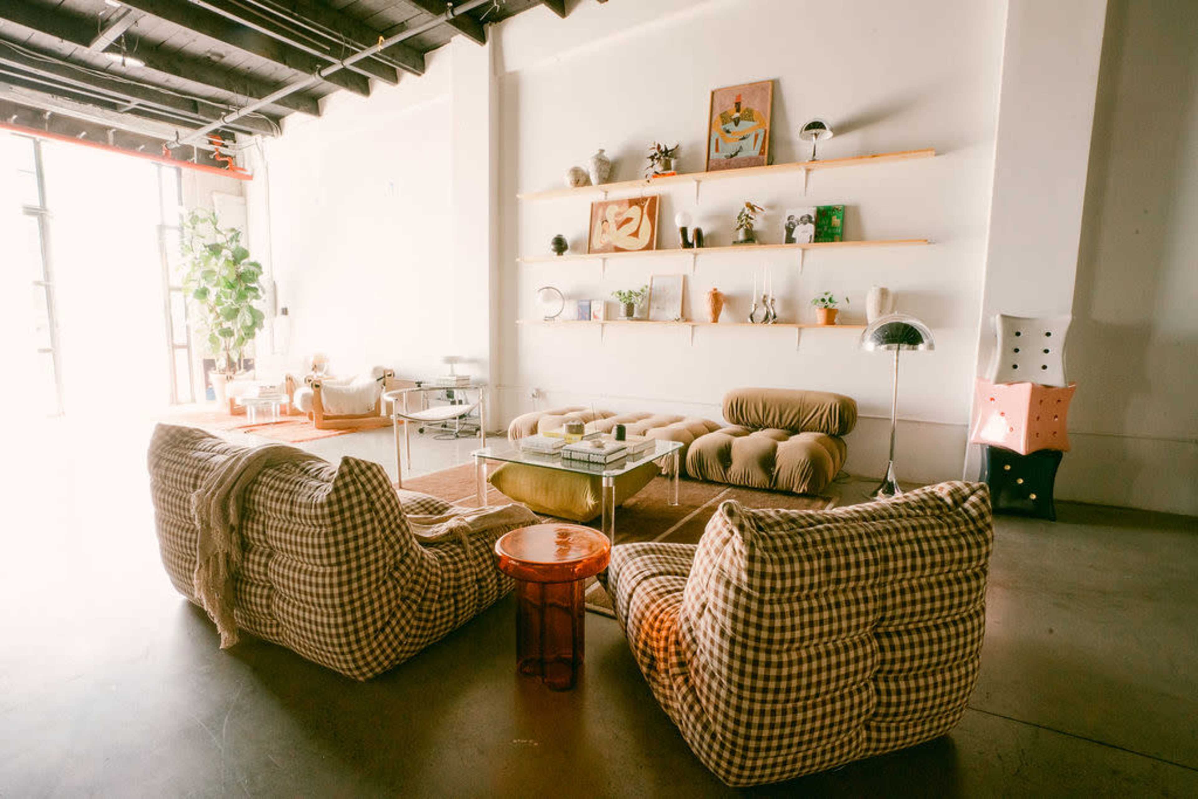 The image shows a modern interior space featuring a cozy seating arrangement with checkered lounge chairs, a low table, and shelves displaying various decorative items.