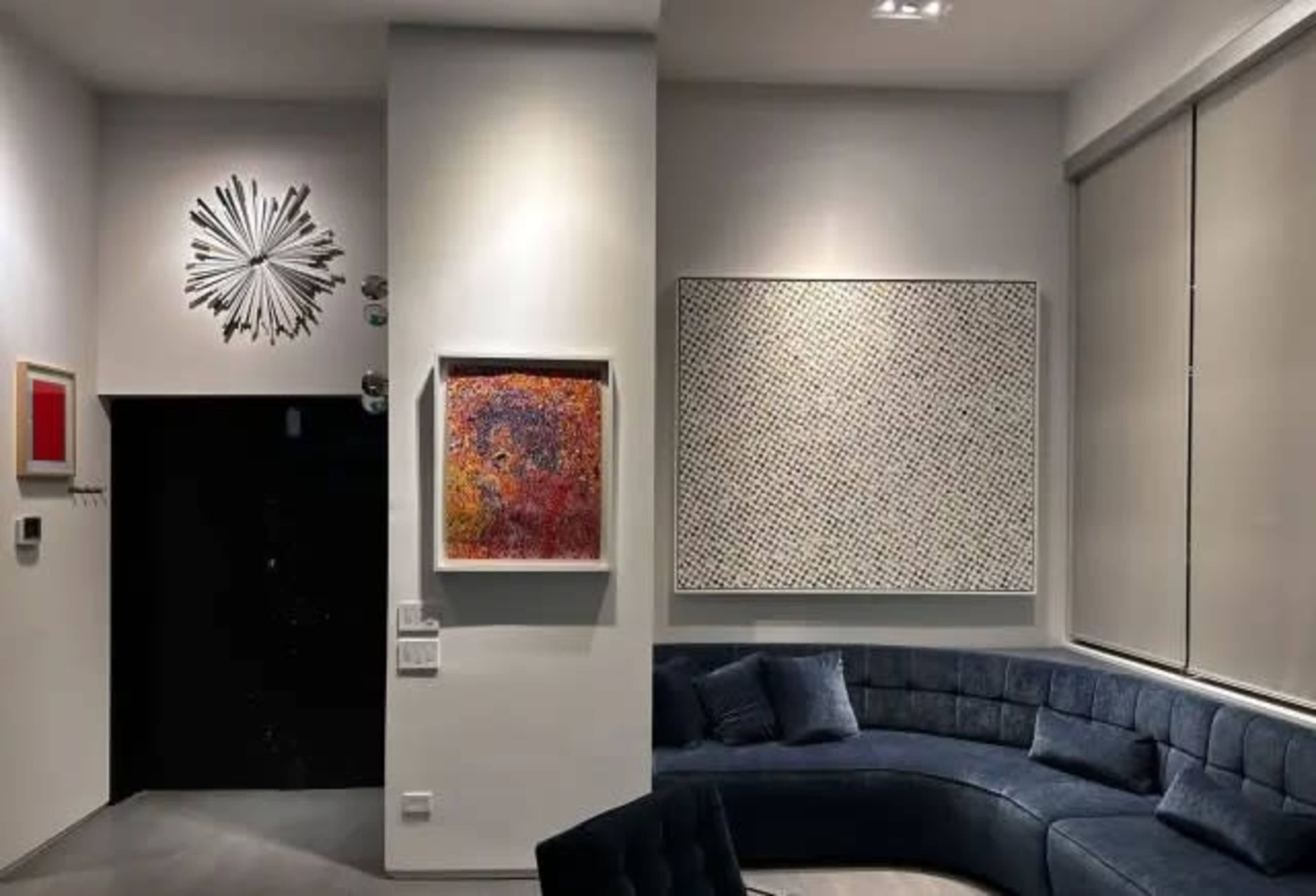 The image shows a modern interior featuring a curved blue sofa, abstract artwork on the walls, and a dark entrance door.