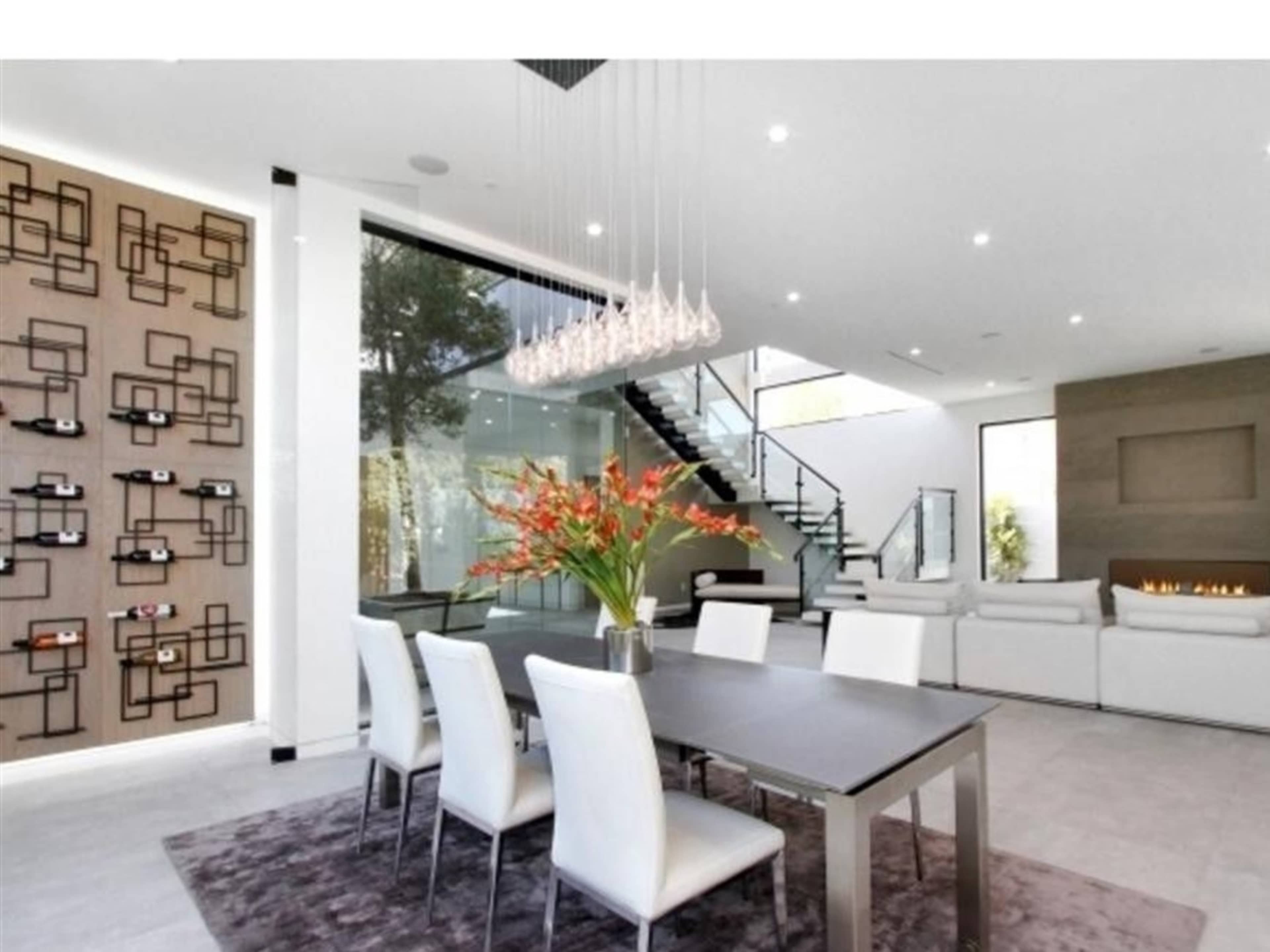 A modern dining area with a large table, white chairs, decorative wall features, and a staircase visible in the background.
