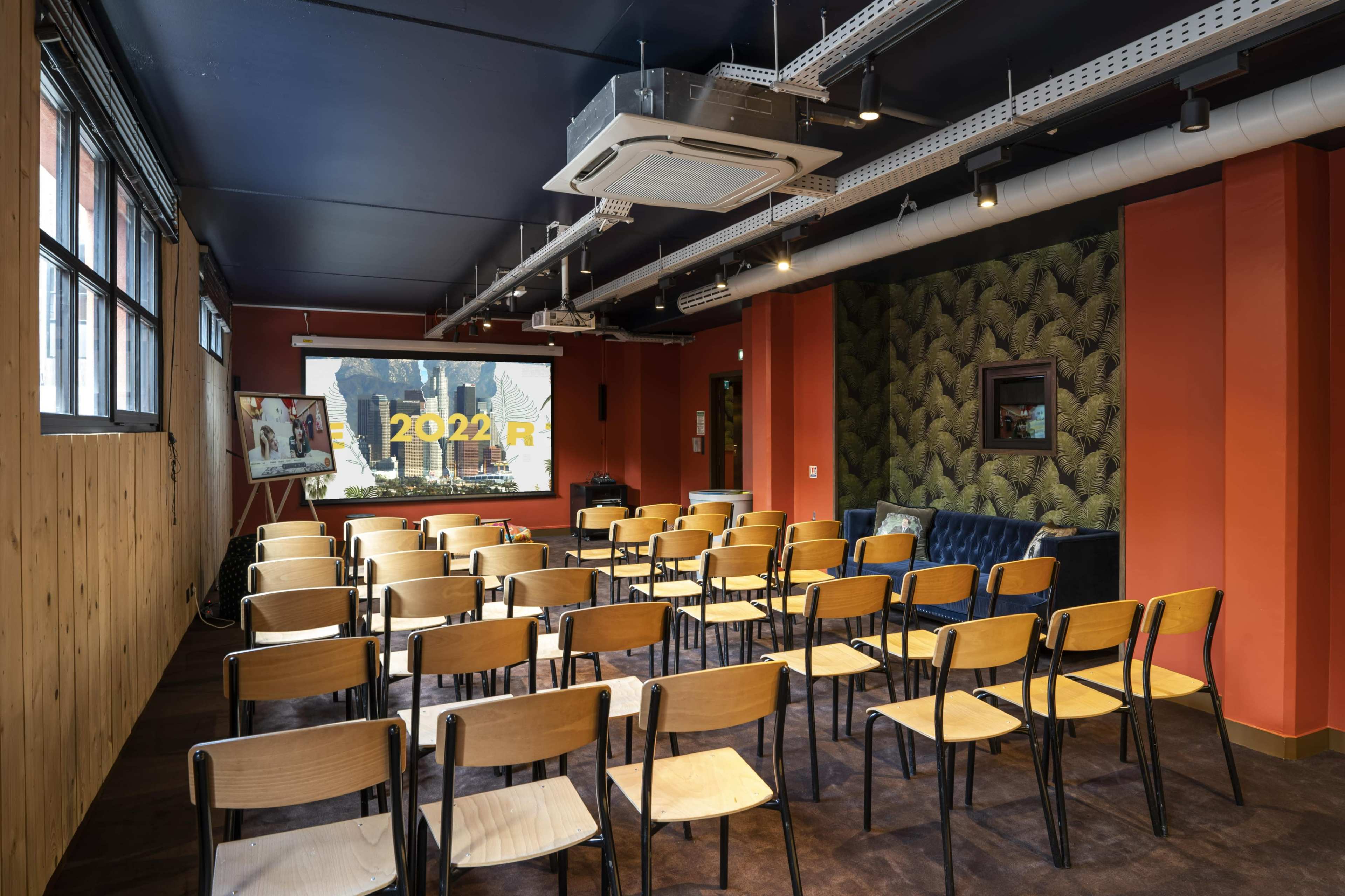 A meeting room set up with rows of empty wooden chairs facing a projector screen that displays the year "2022."