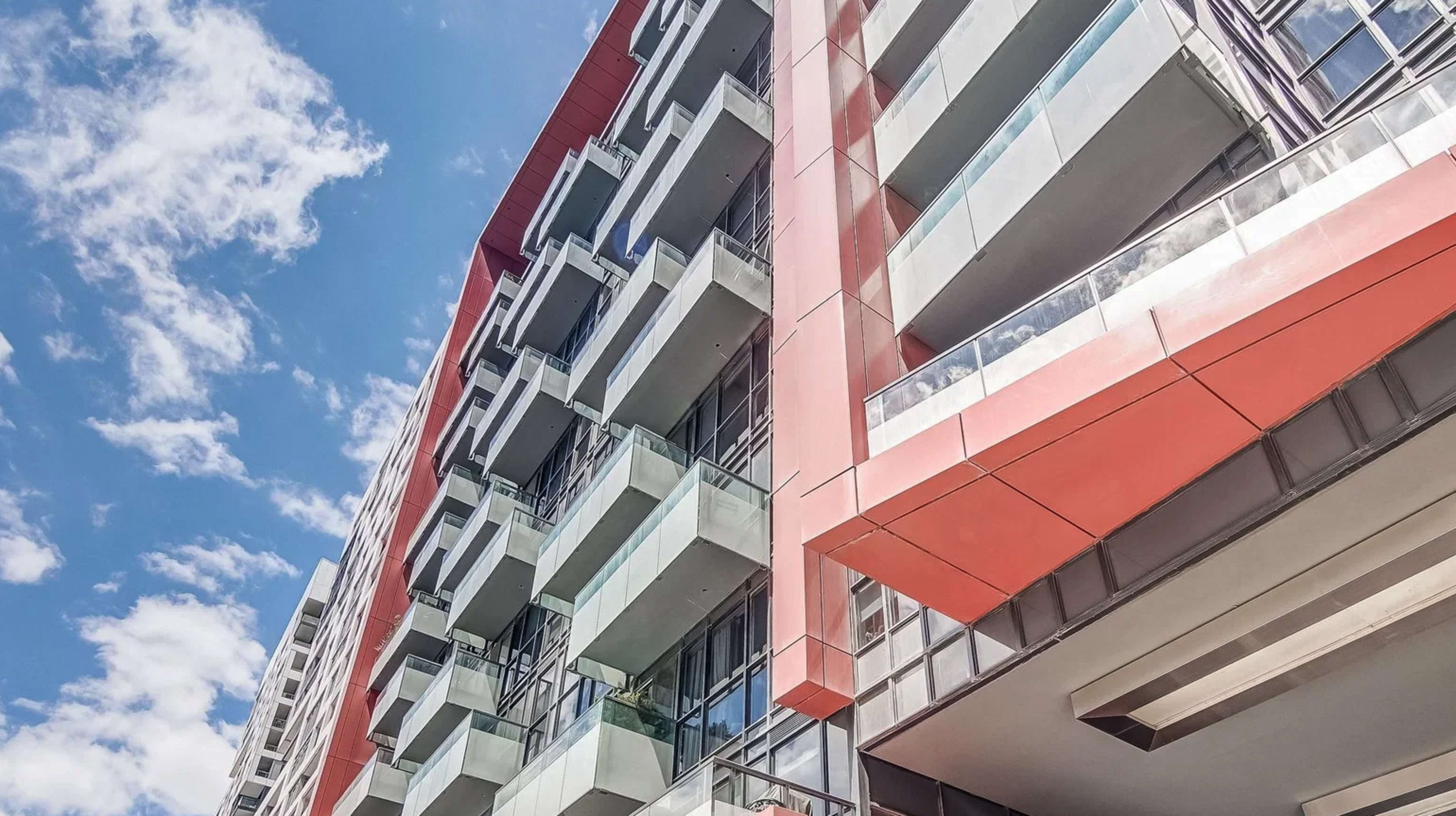 The image shows a modern multi-story building with a prominent red and glass facade against a blue sky.