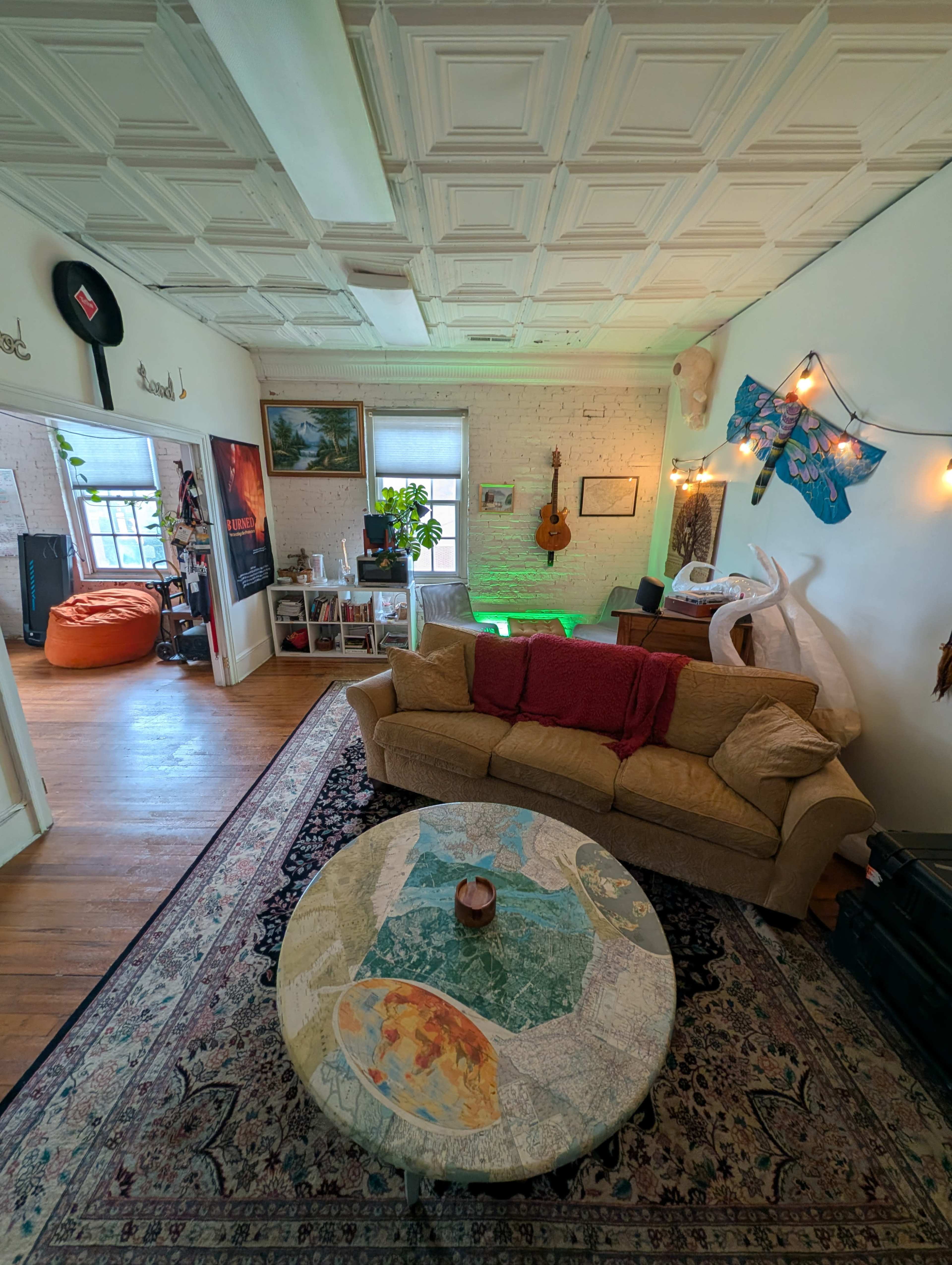The image shows a cozy living room with a beige couch, a coffee table featuring a map design, and various decorative elements on the walls and furniture.