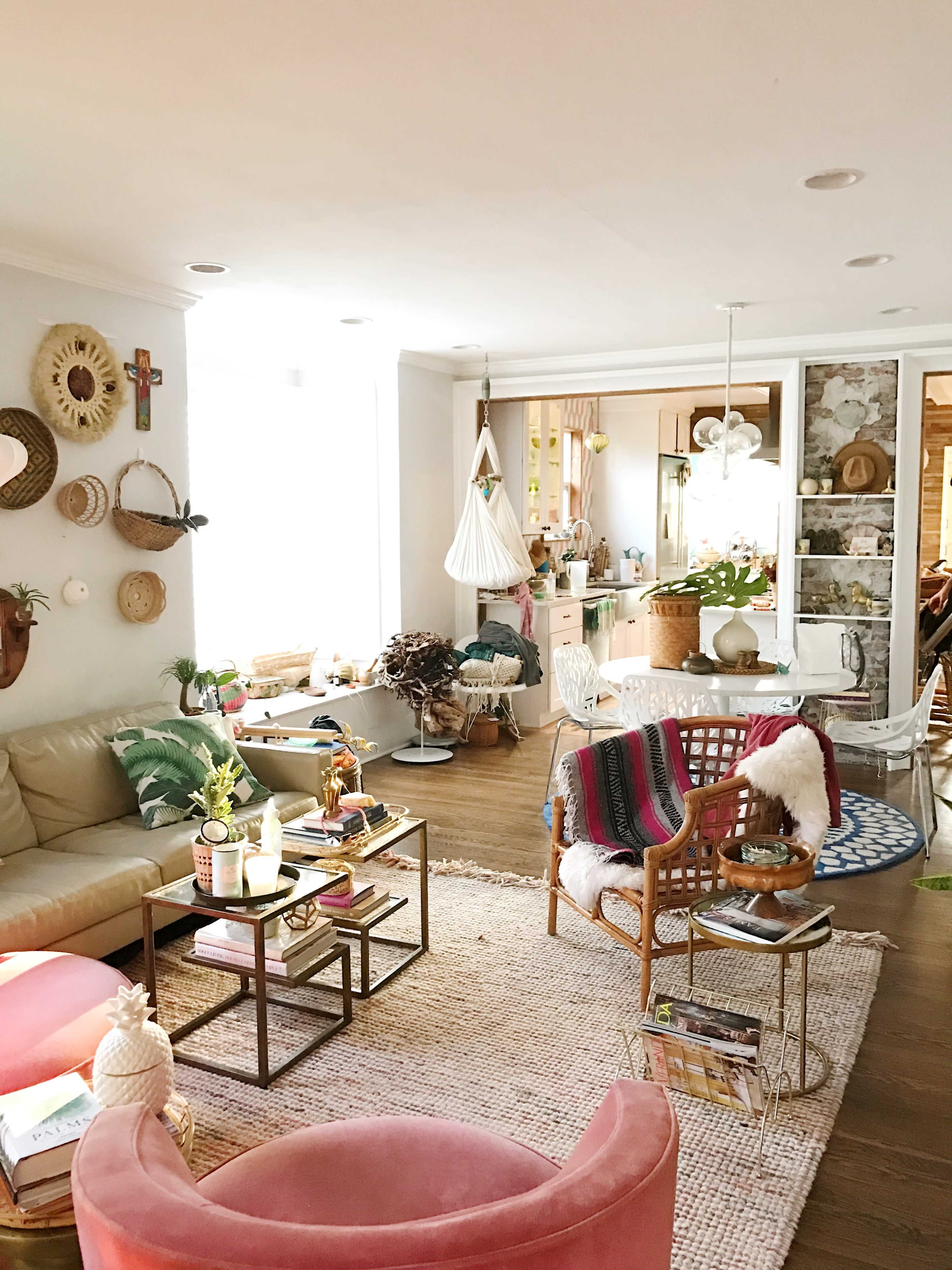 A bright living room features a beige sofa, colorful decor, and a variety of plants arranged around a central rug.