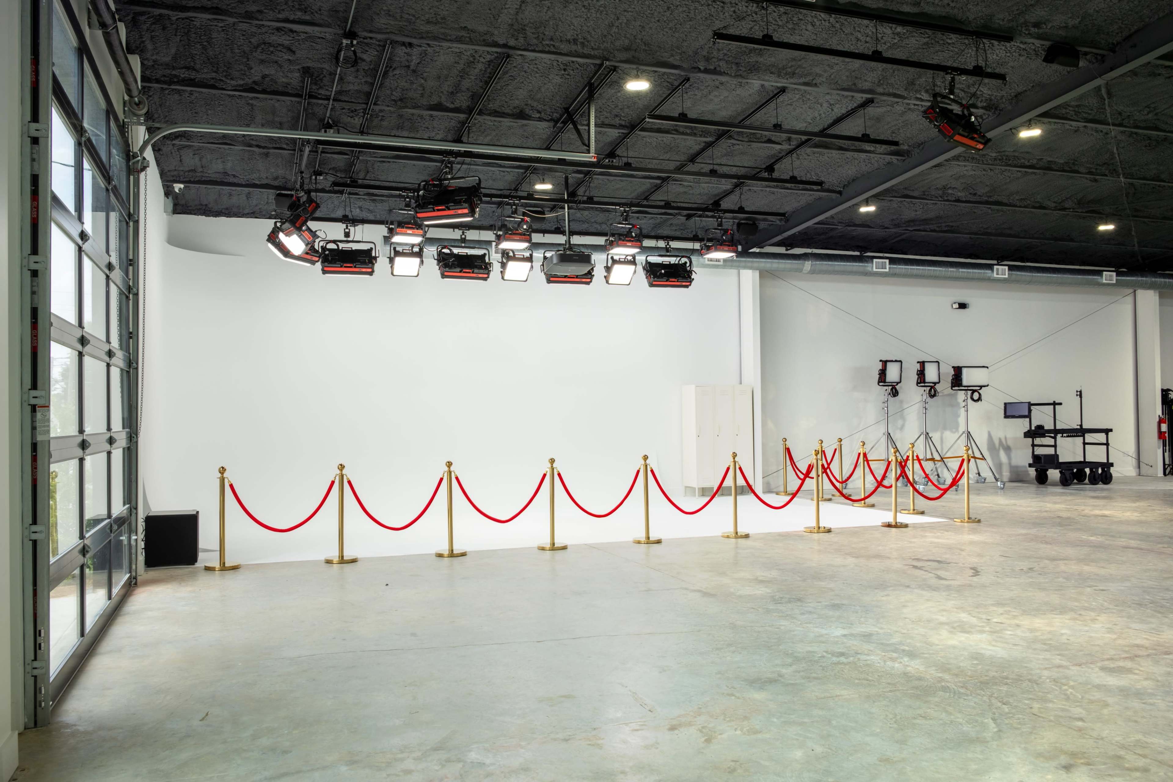 An empty studio space is equipped with lighting fixtures and a red carpet barrier separating the area.