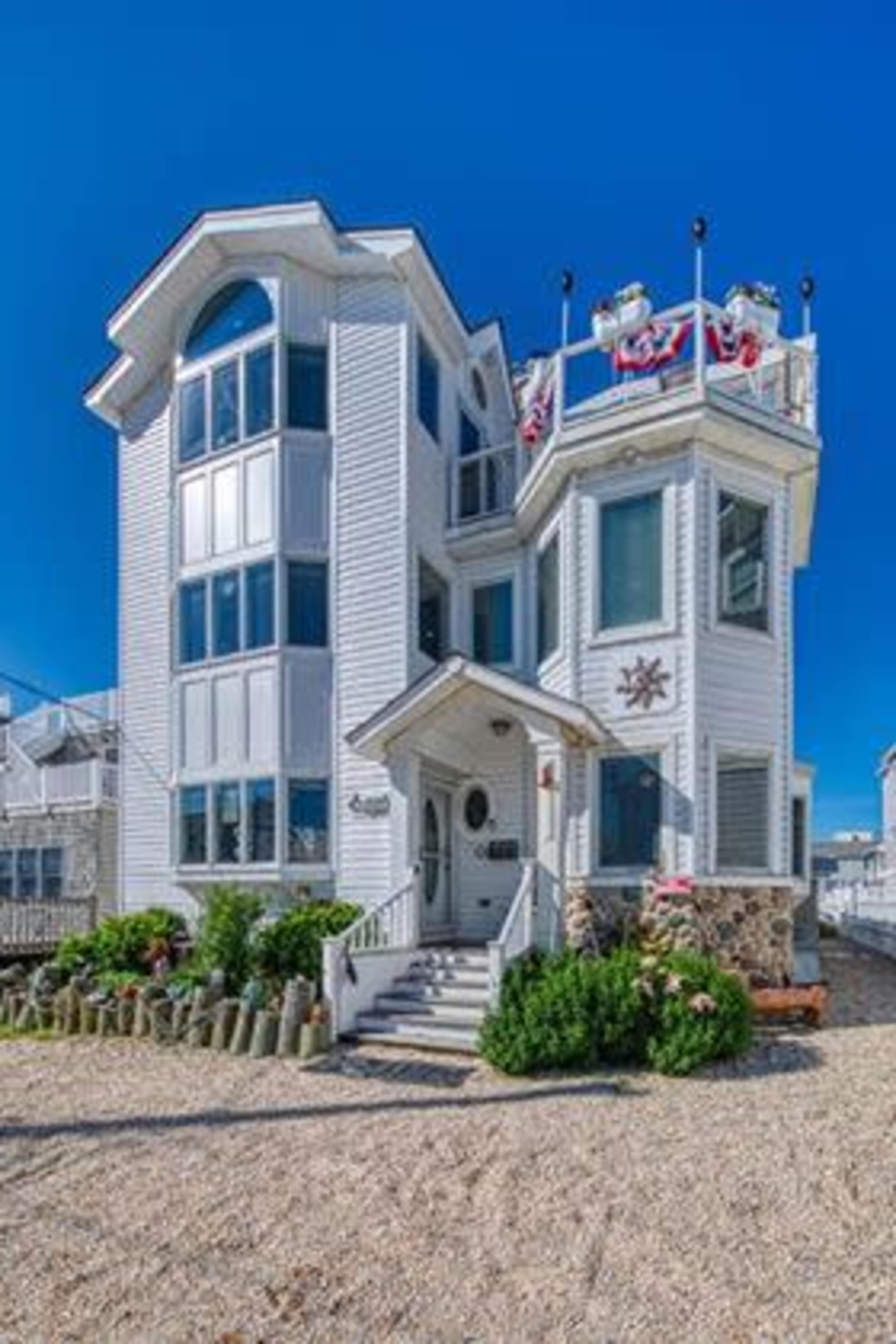 A three-story seaside house with a modern design, featuring large windows and a decorative rooftop.
