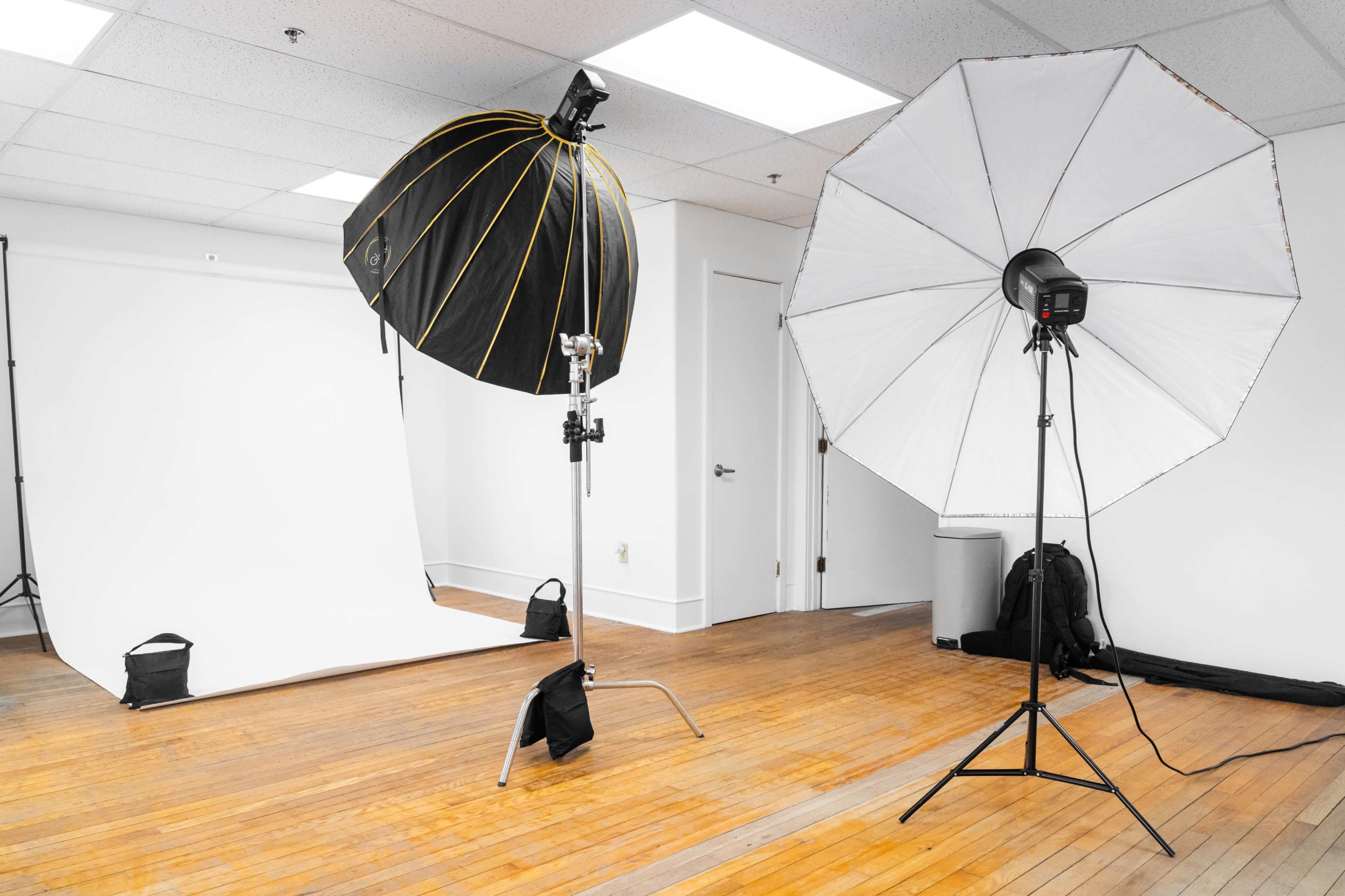 A photography studio equipped with two large softbox light sources, a mirror, and a blank backdrop in a well-lit room.