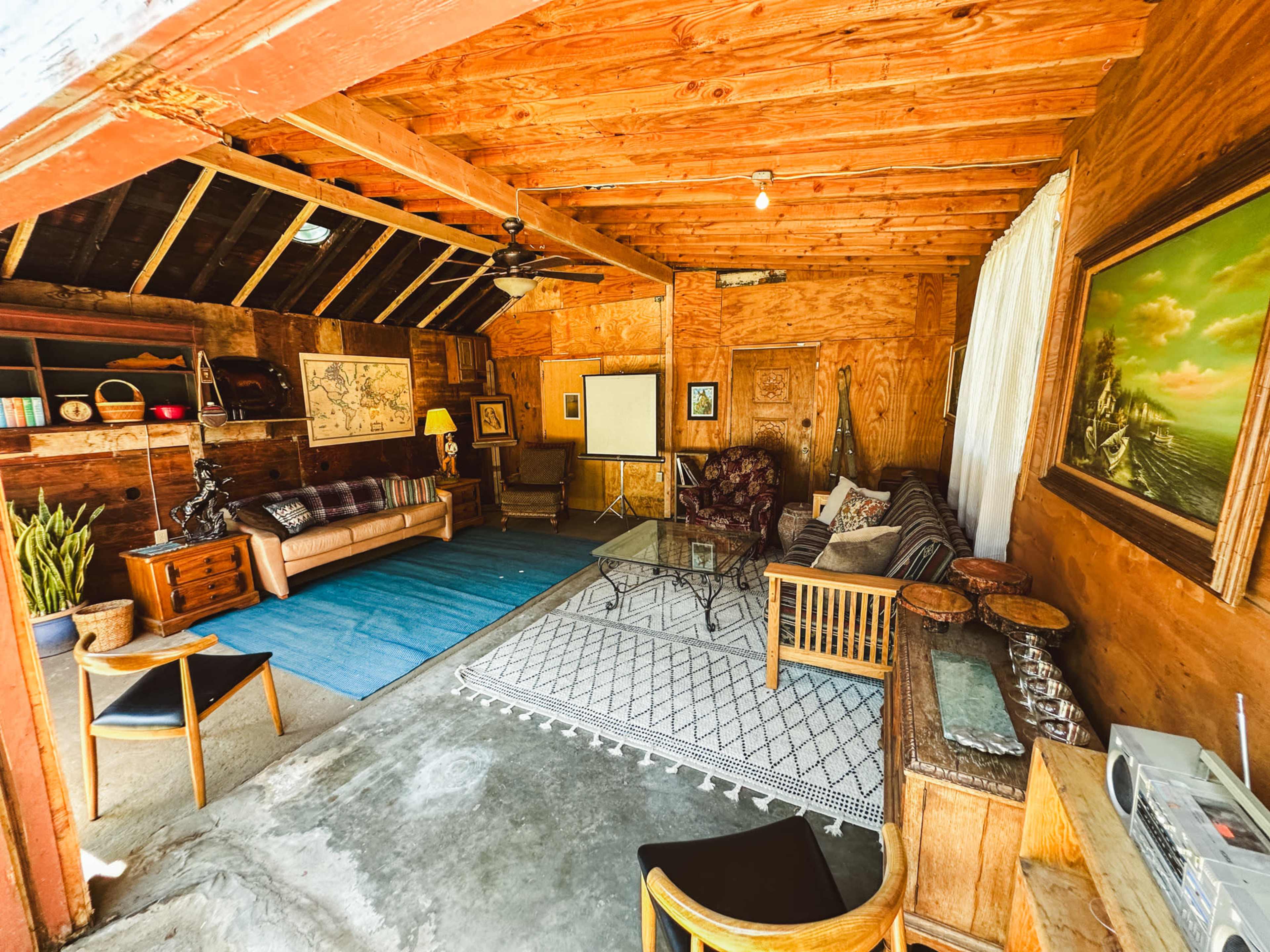 A wooden interior space with a seating area, a large rug, and various decorative items against the walls.