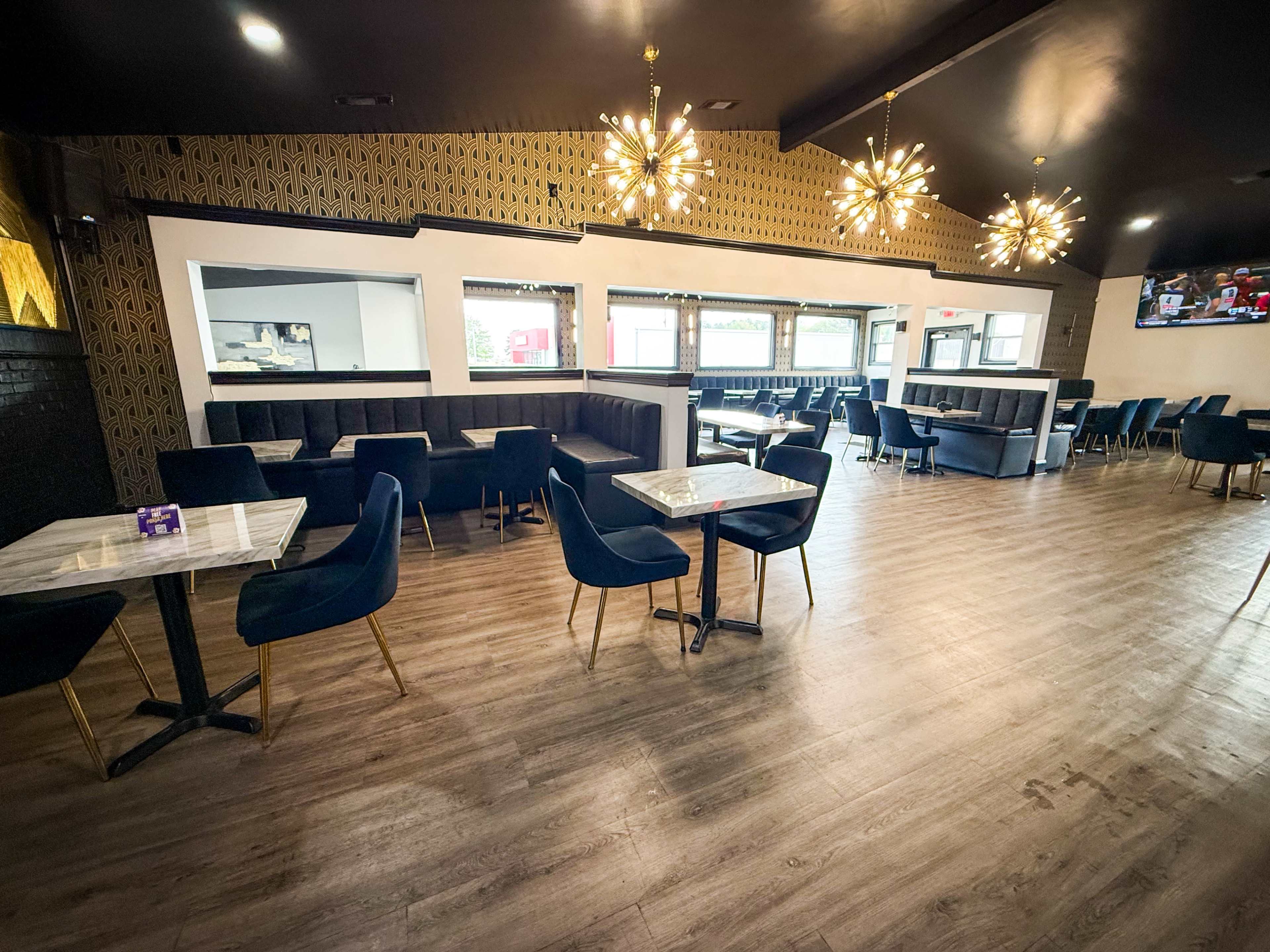 The image shows a modern restaurant interior with dark furniture, marble-topped tables, and decorative lighting fixtures.