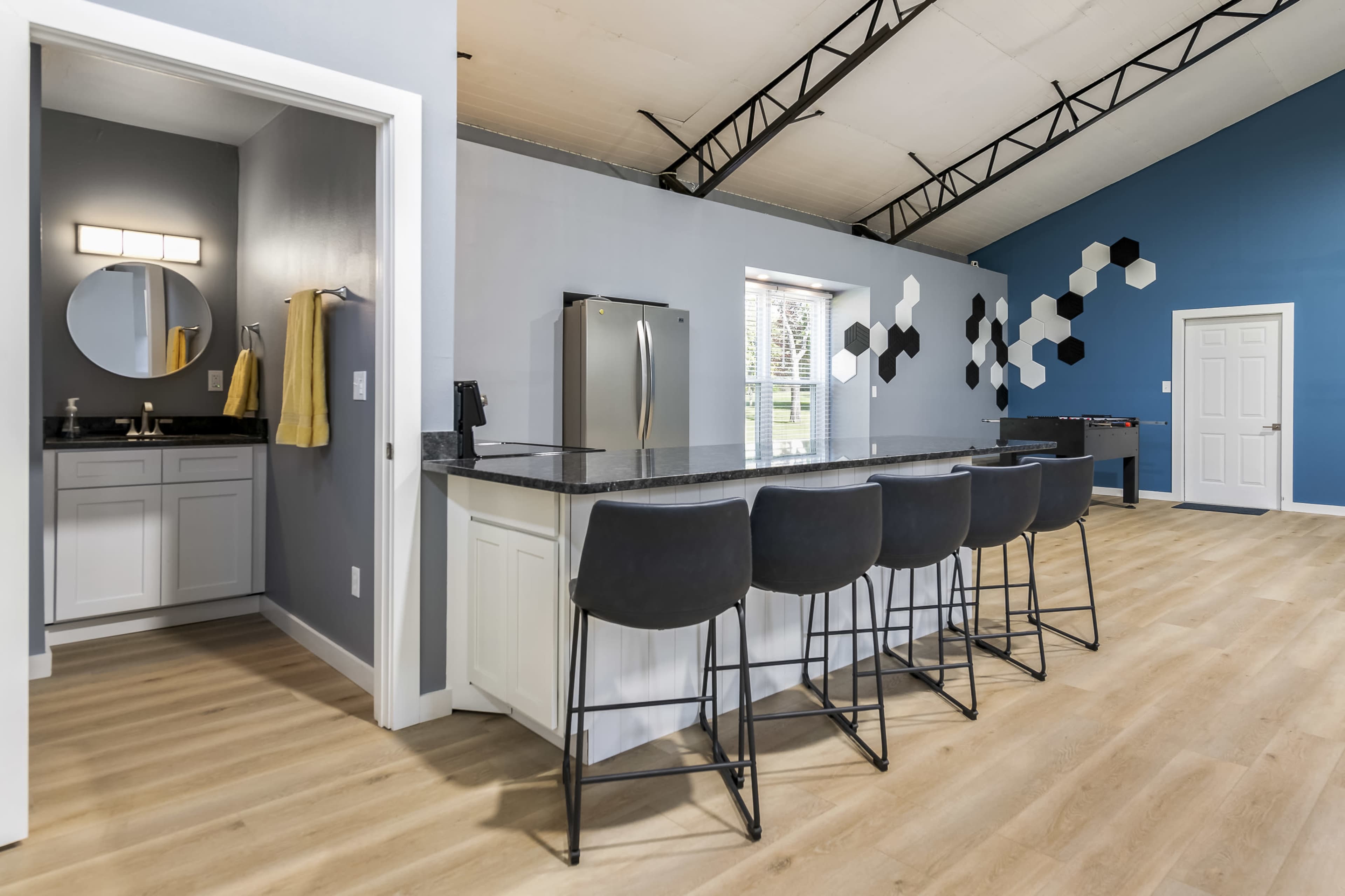 A modern kitchen area featuring a large island with black bar stools, connected to a space that includes a bathroom and colorful wall decor.