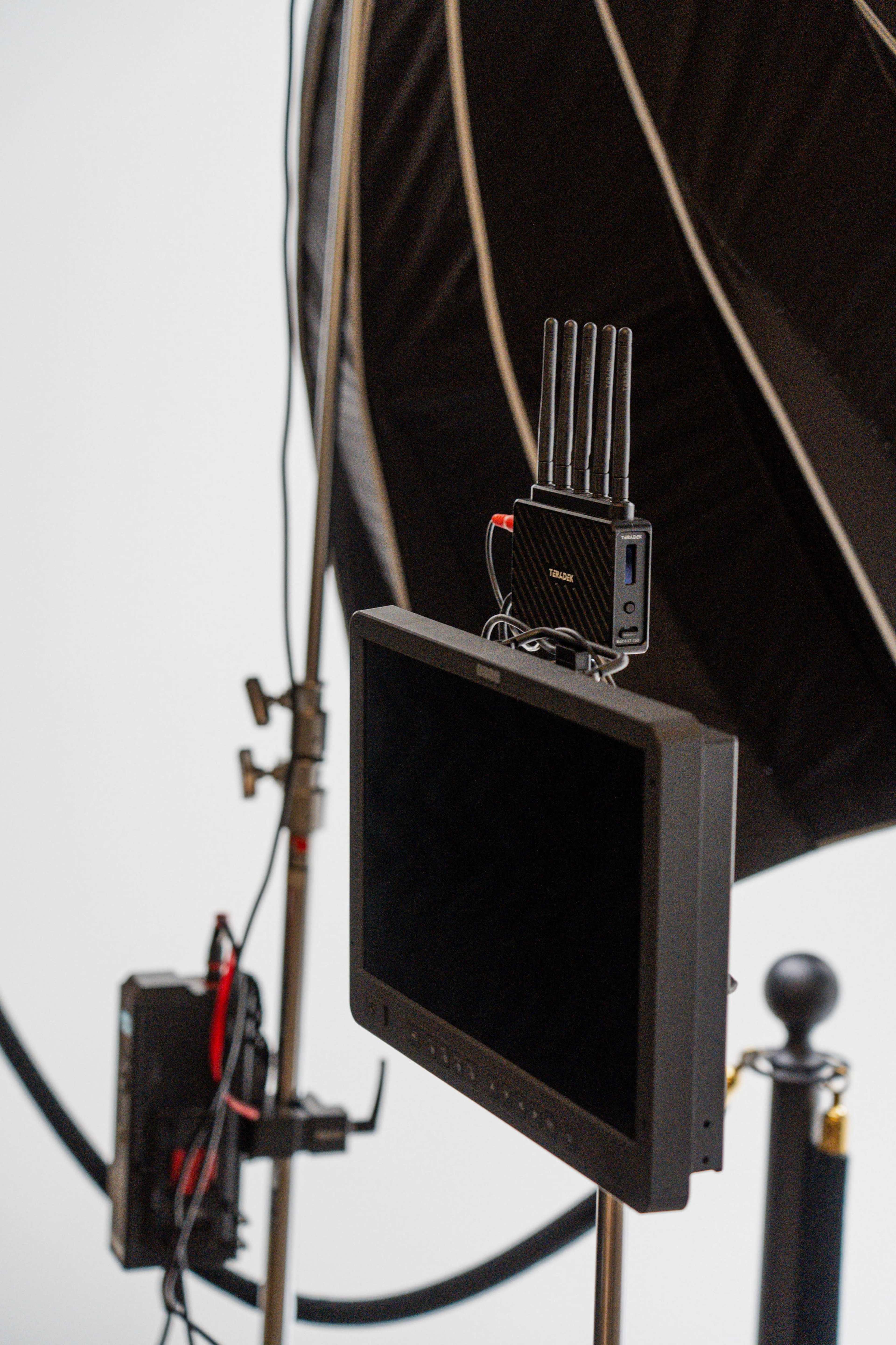 A monitor mounted on a stand with a wireless device on top, alongside a large softbox lighting setup.
