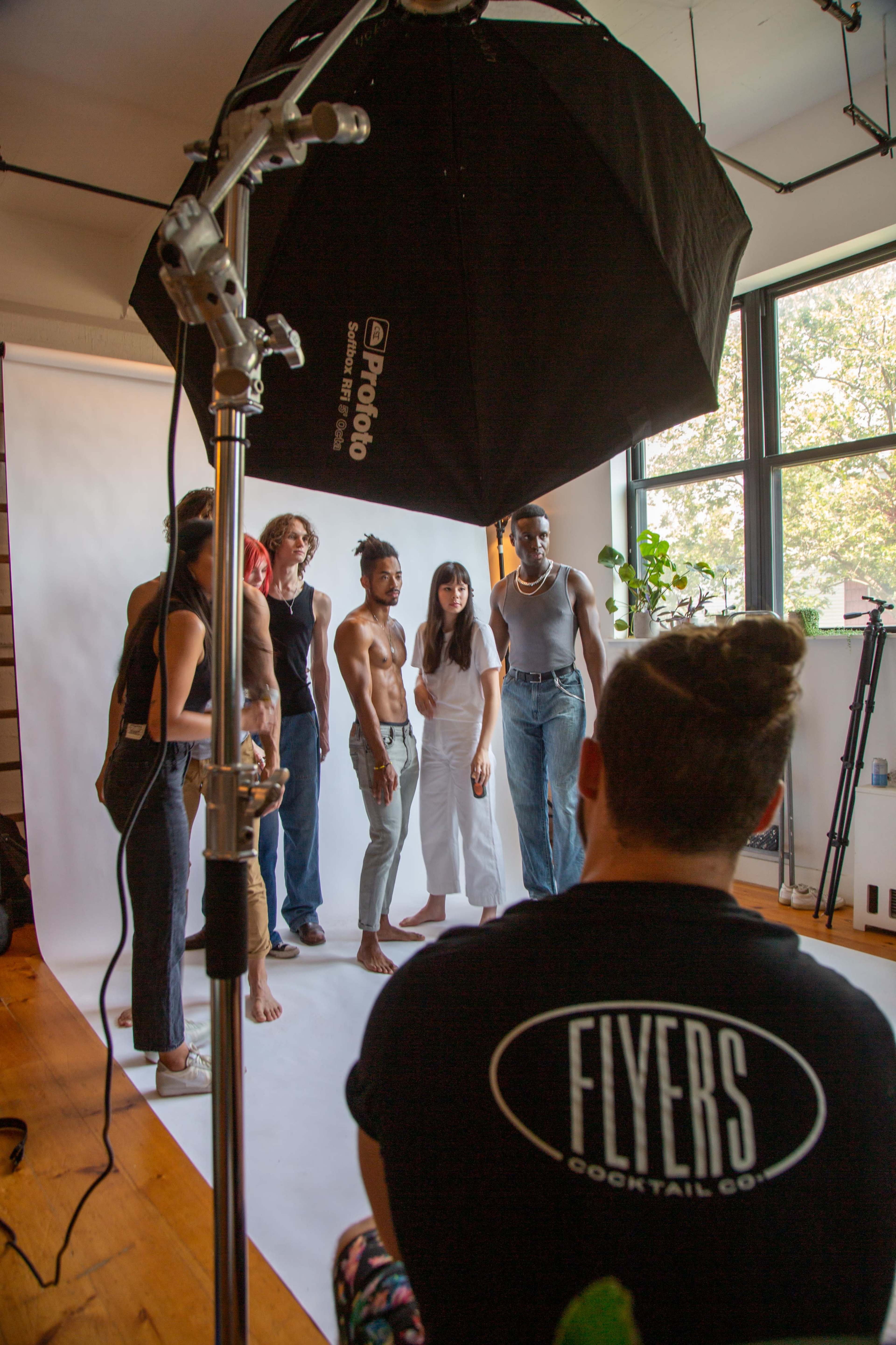 A group of seven people is posing for a photoshoot in a brightly lit studio with a large softbox overhead.