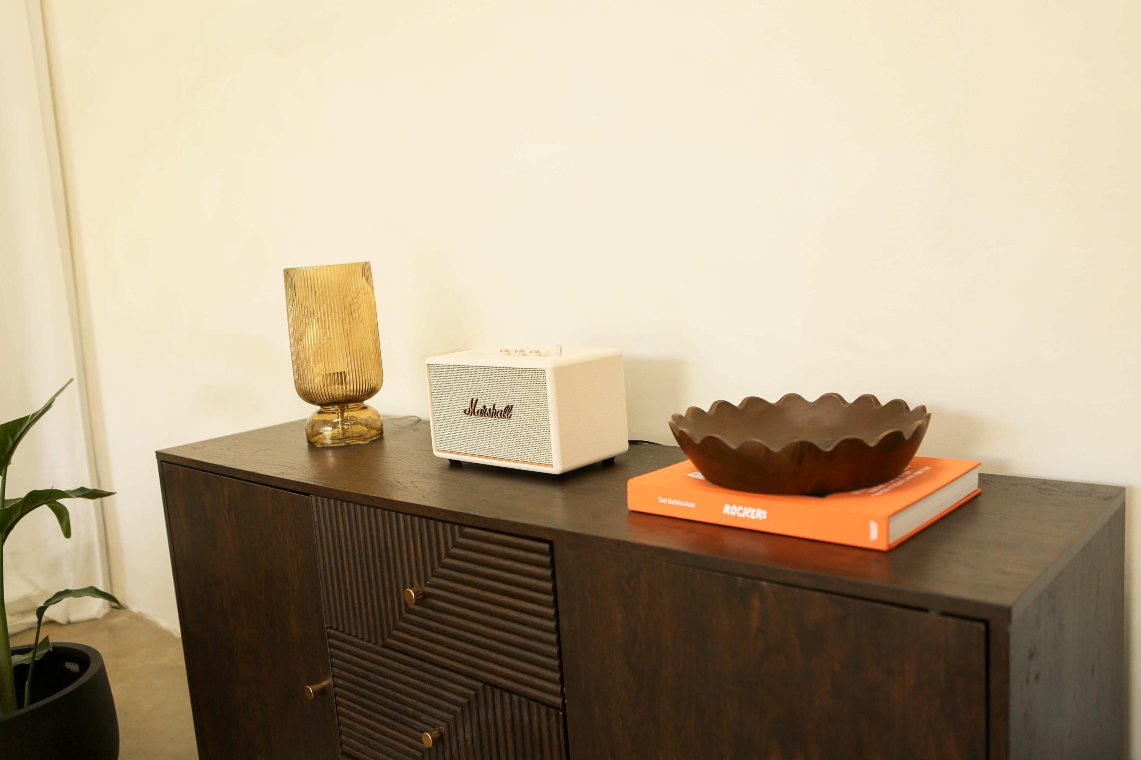 A wooden sideboard displays a lamp, a Marshall speaker, a decorative bowl, and two books.