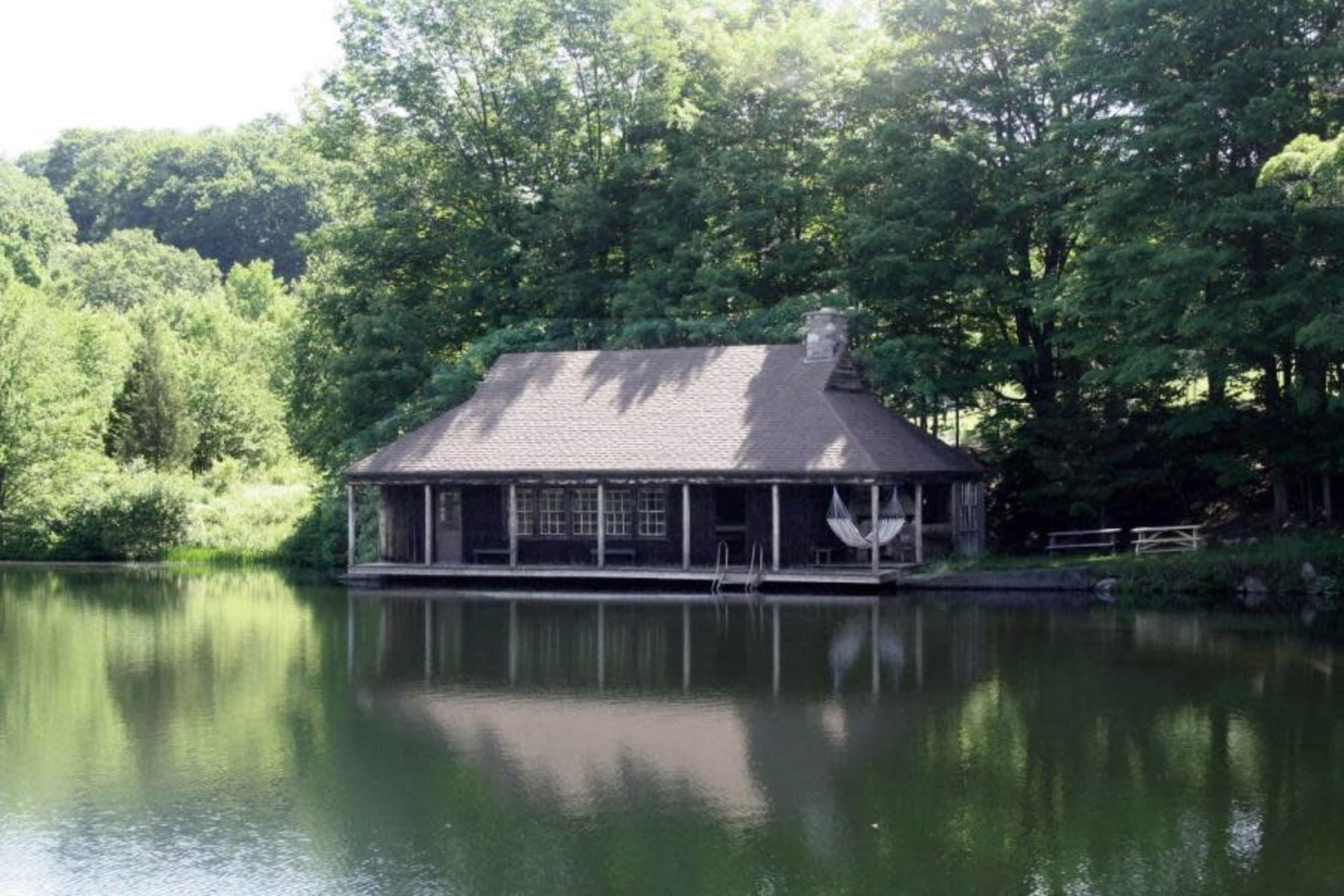 A wooden cabin sits by a calm lake, surrounded by trees.