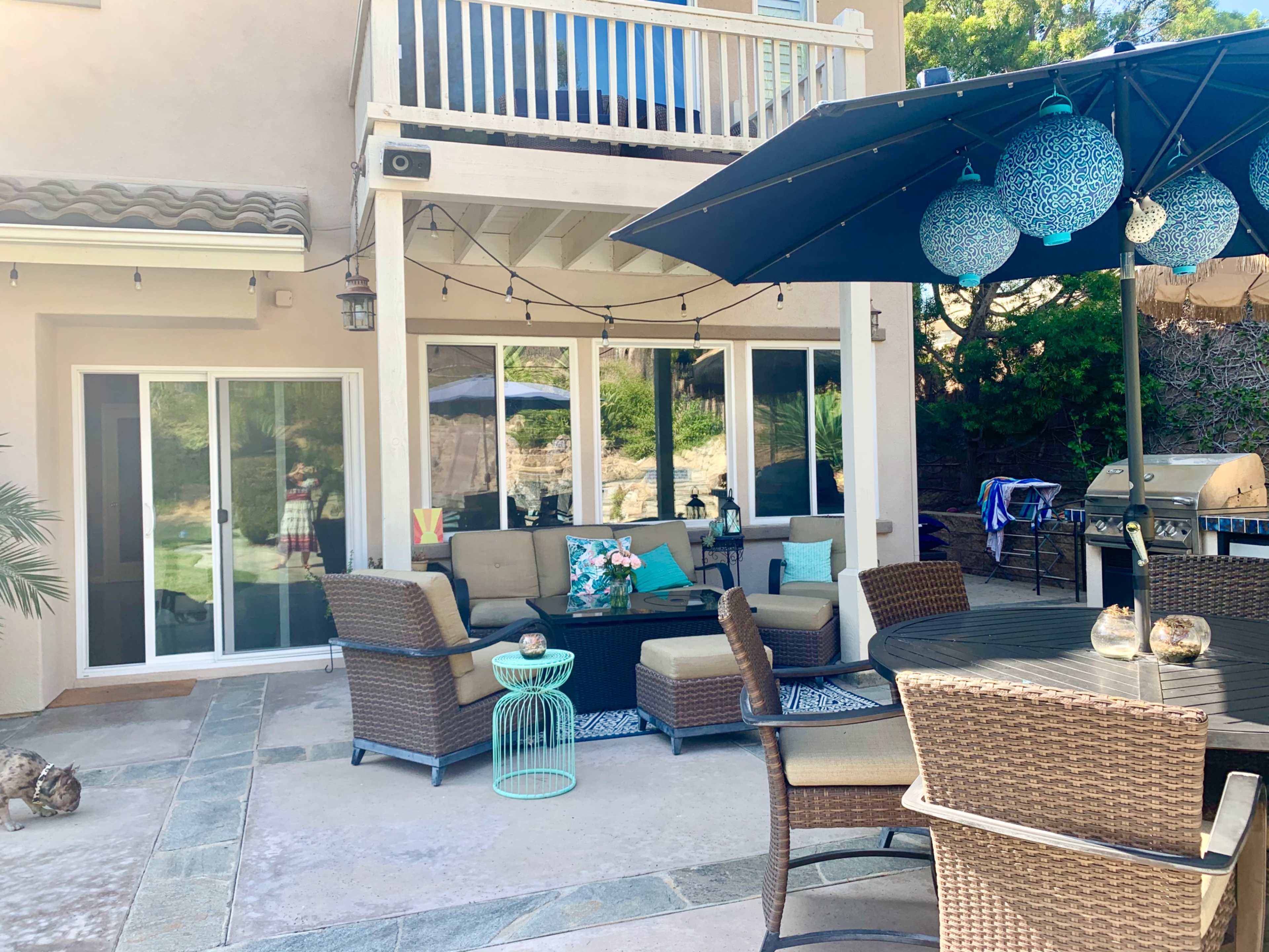 A backyard patio area with a seating arrangement, an umbrella, and a barbecue grill.